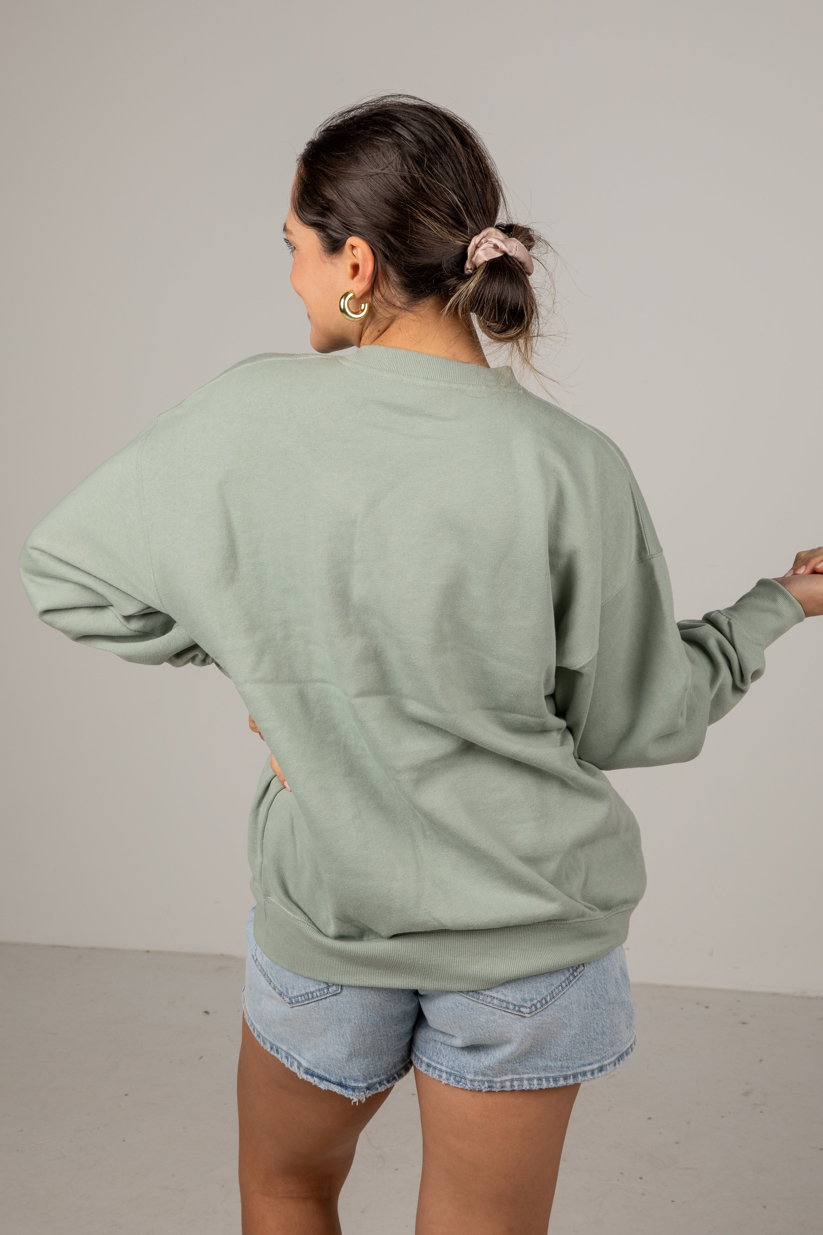 Person wearing a light green sweatshirt and denim shorts against a plain background