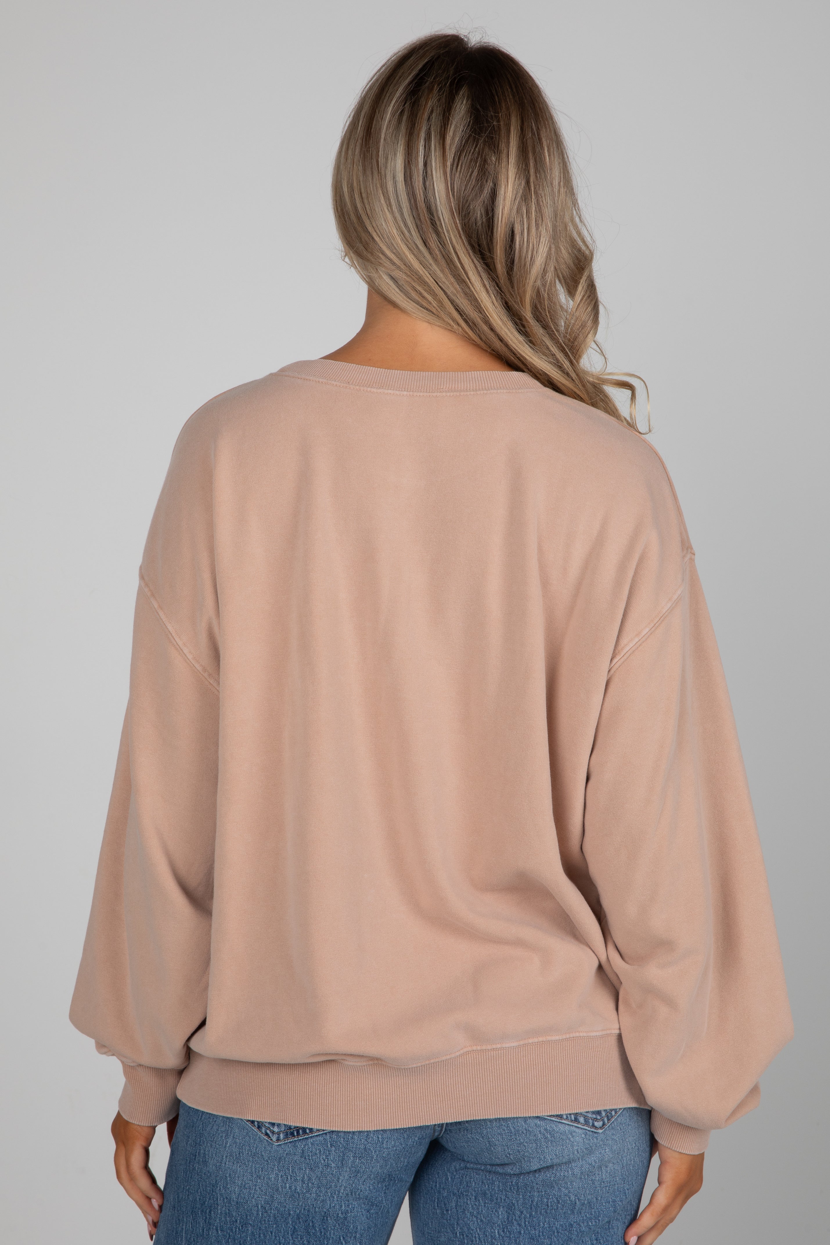 Person wearing a beige sweater and blue jeans on a plain background