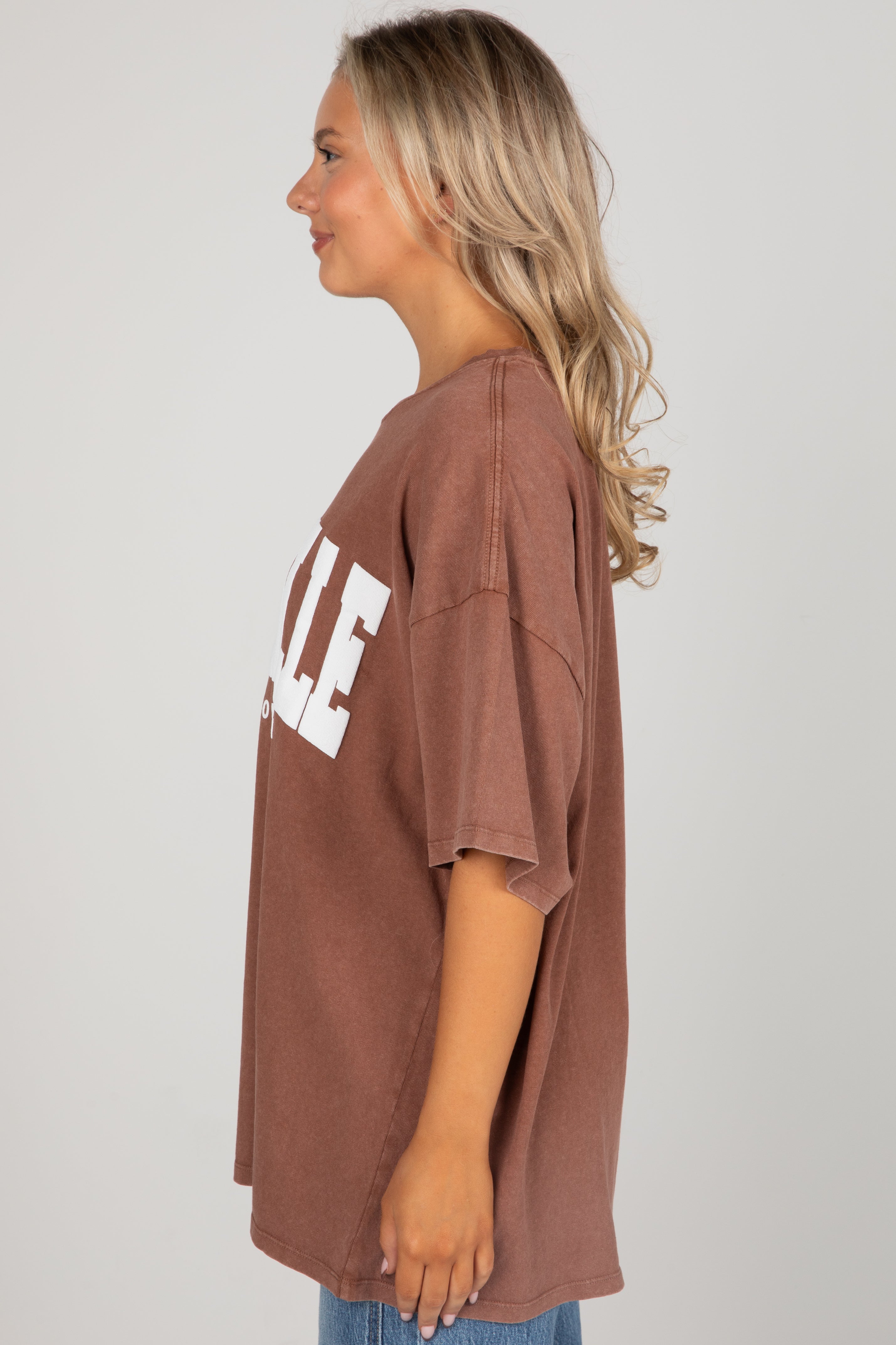 Woman wearing a brown oversized t-shirt with white text on a plain background