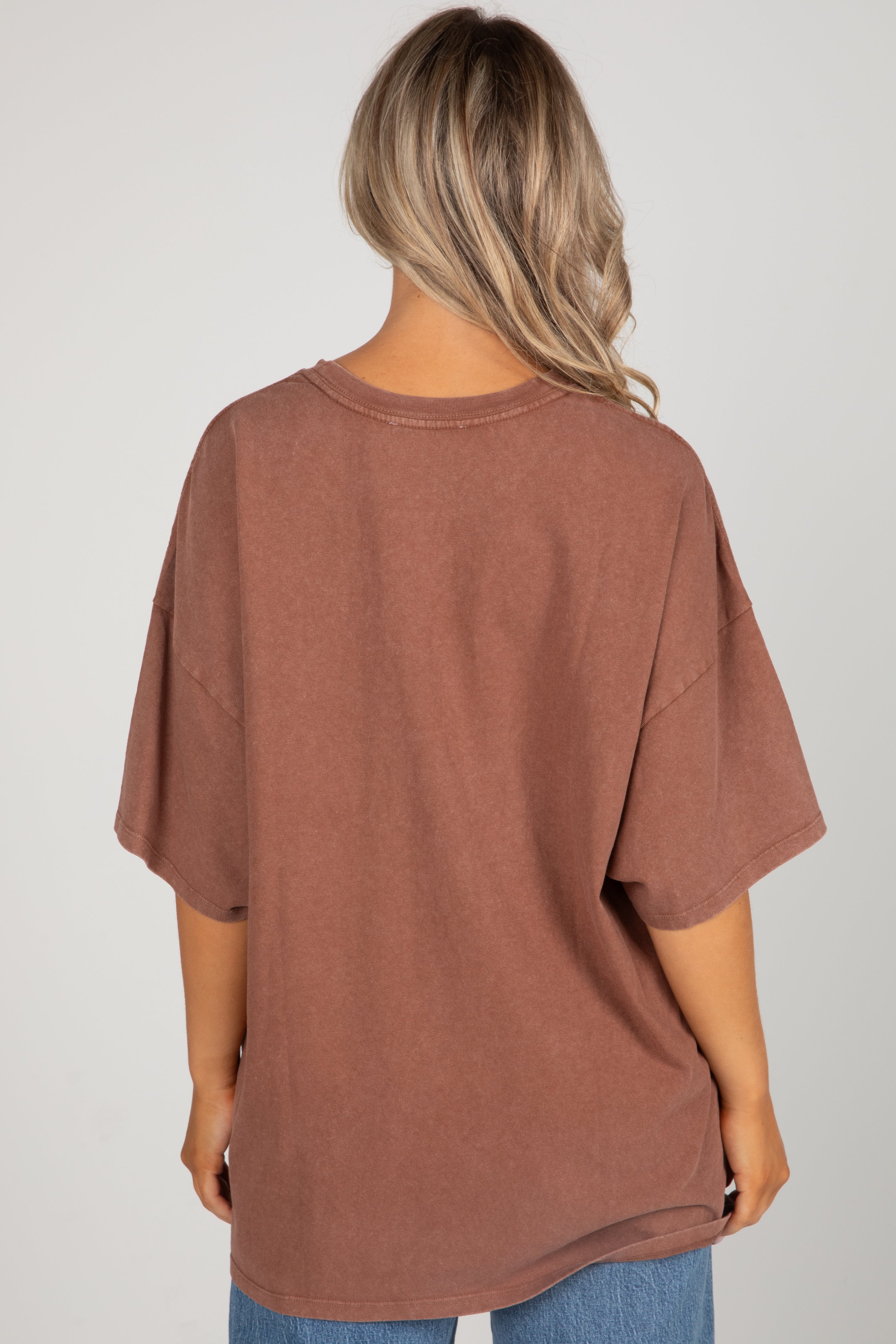 Person wearing a brown oversized t-shirt on a plain background