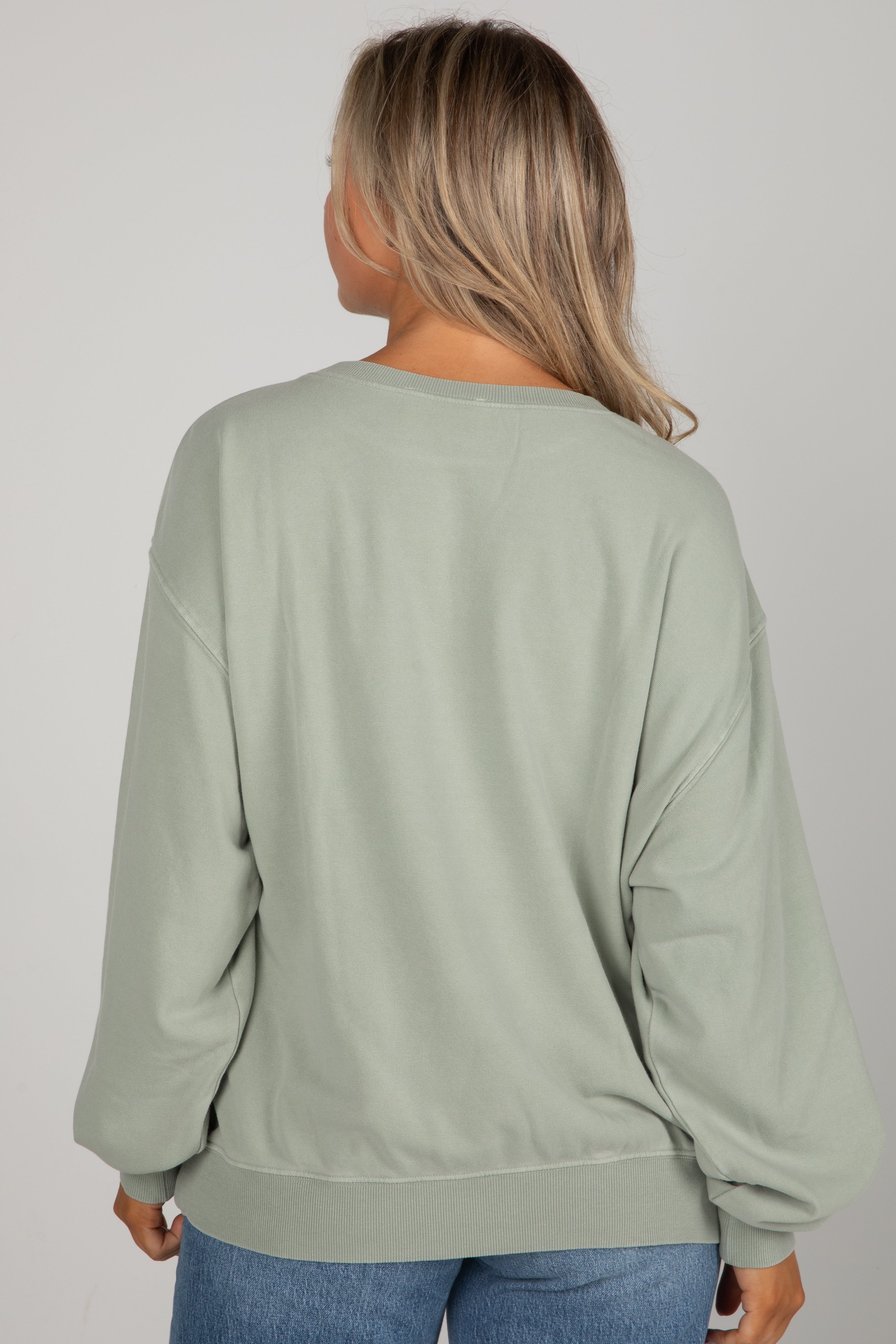 Person wearing a light green sweatshirt and blue jeans on a plain background