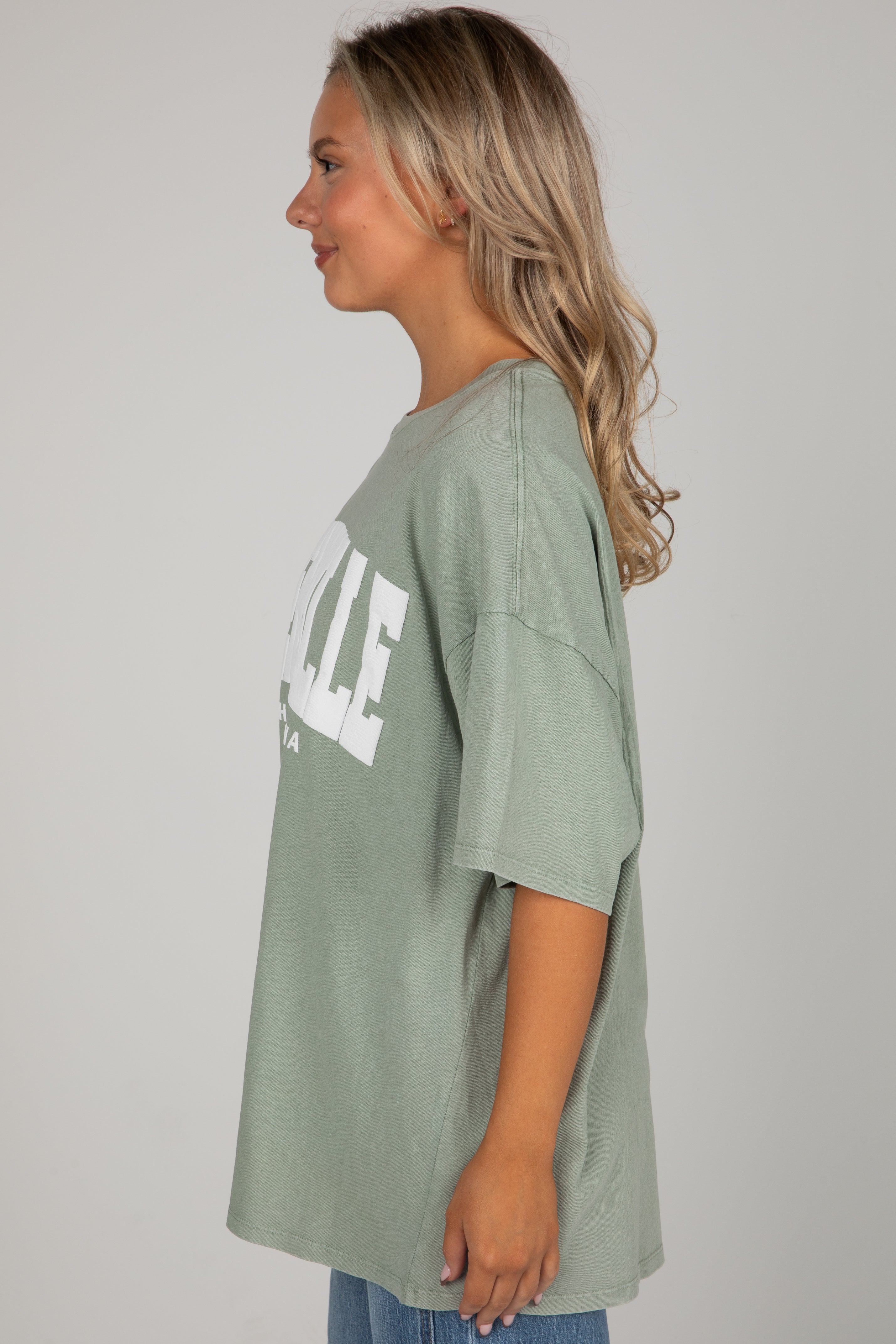 Woman wearing a green oversized t-shirt with text on a plain background