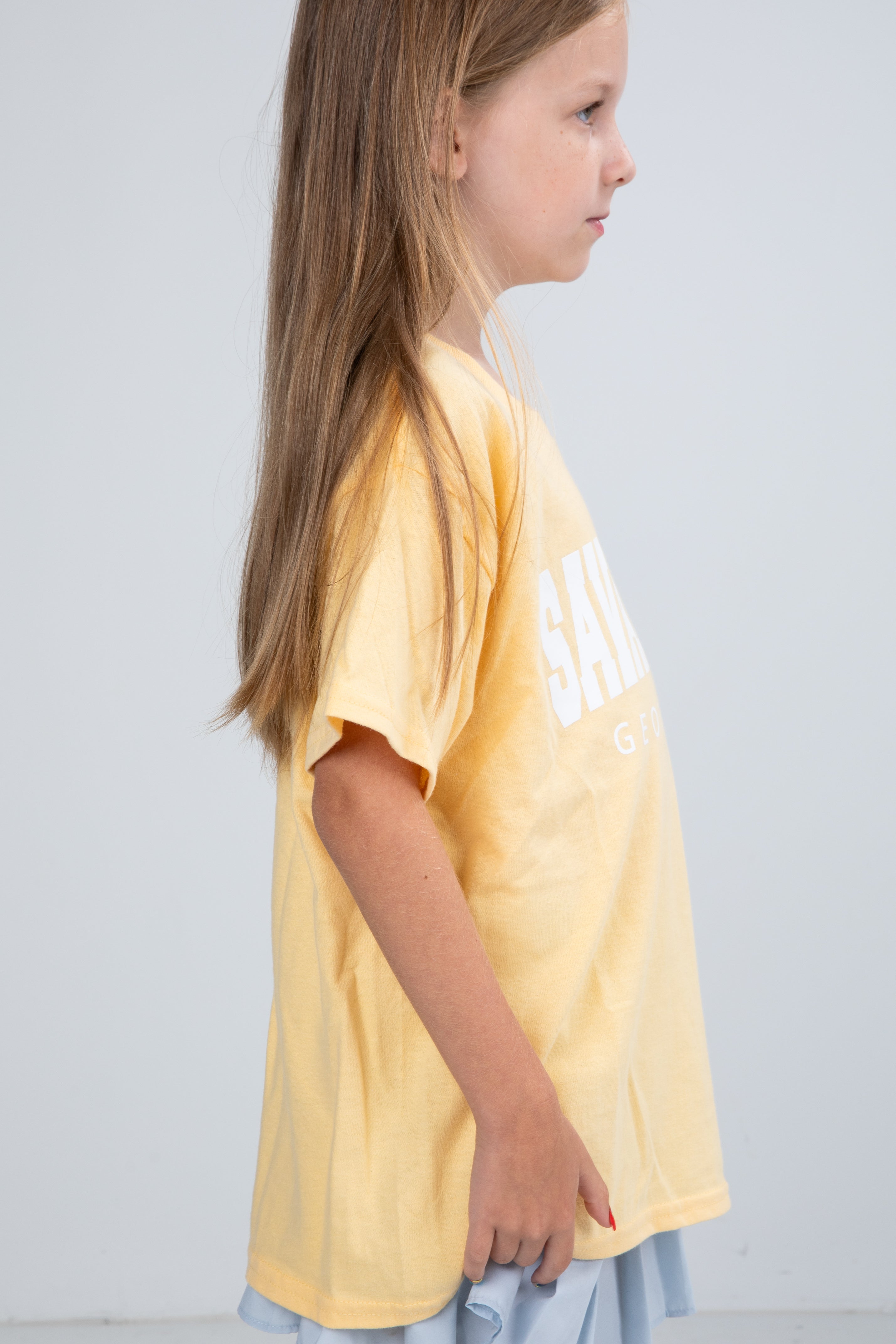Young girl wearing a yellow t-shirt with text on a plain background
