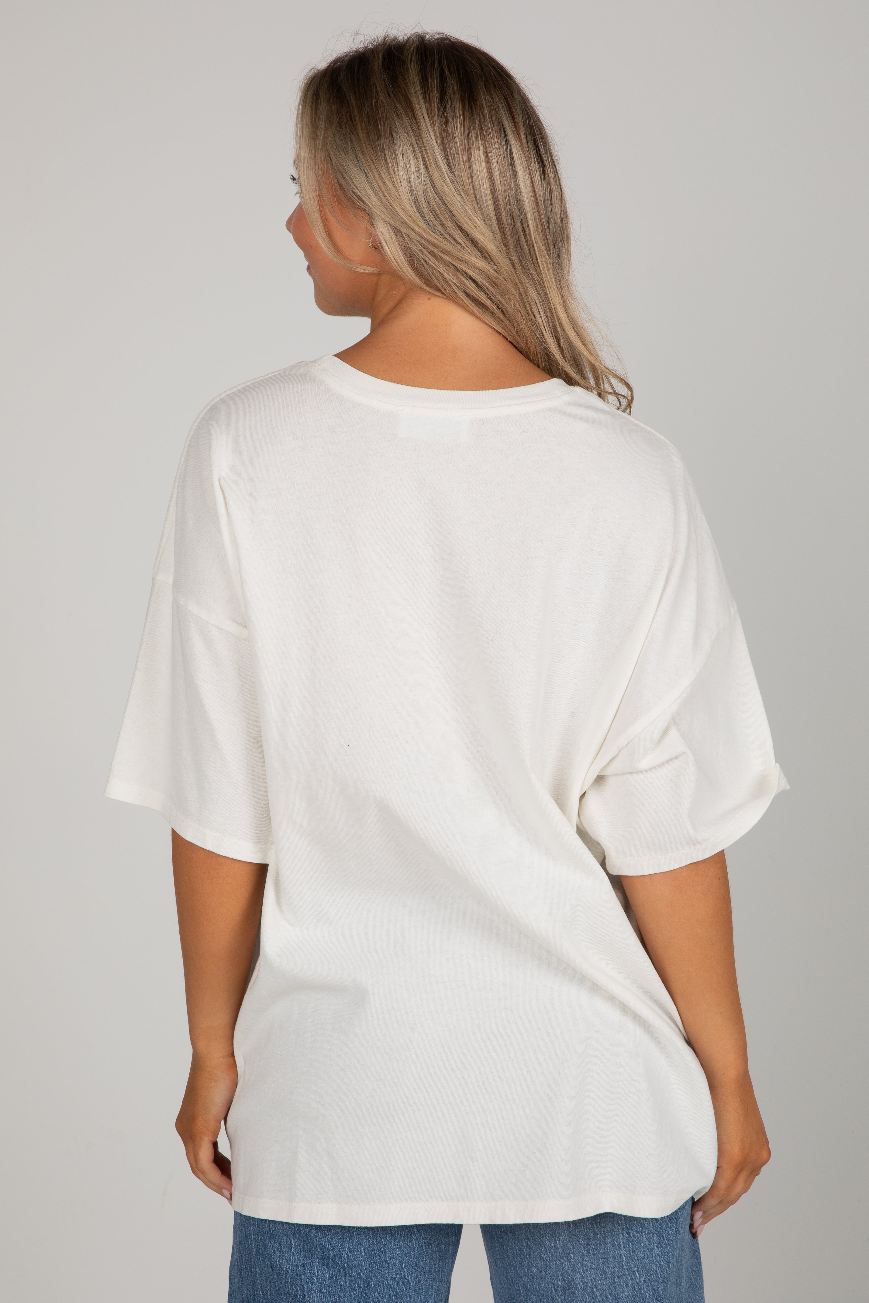Person wearing a white oversized t-shirt and blue jeans on a gray background