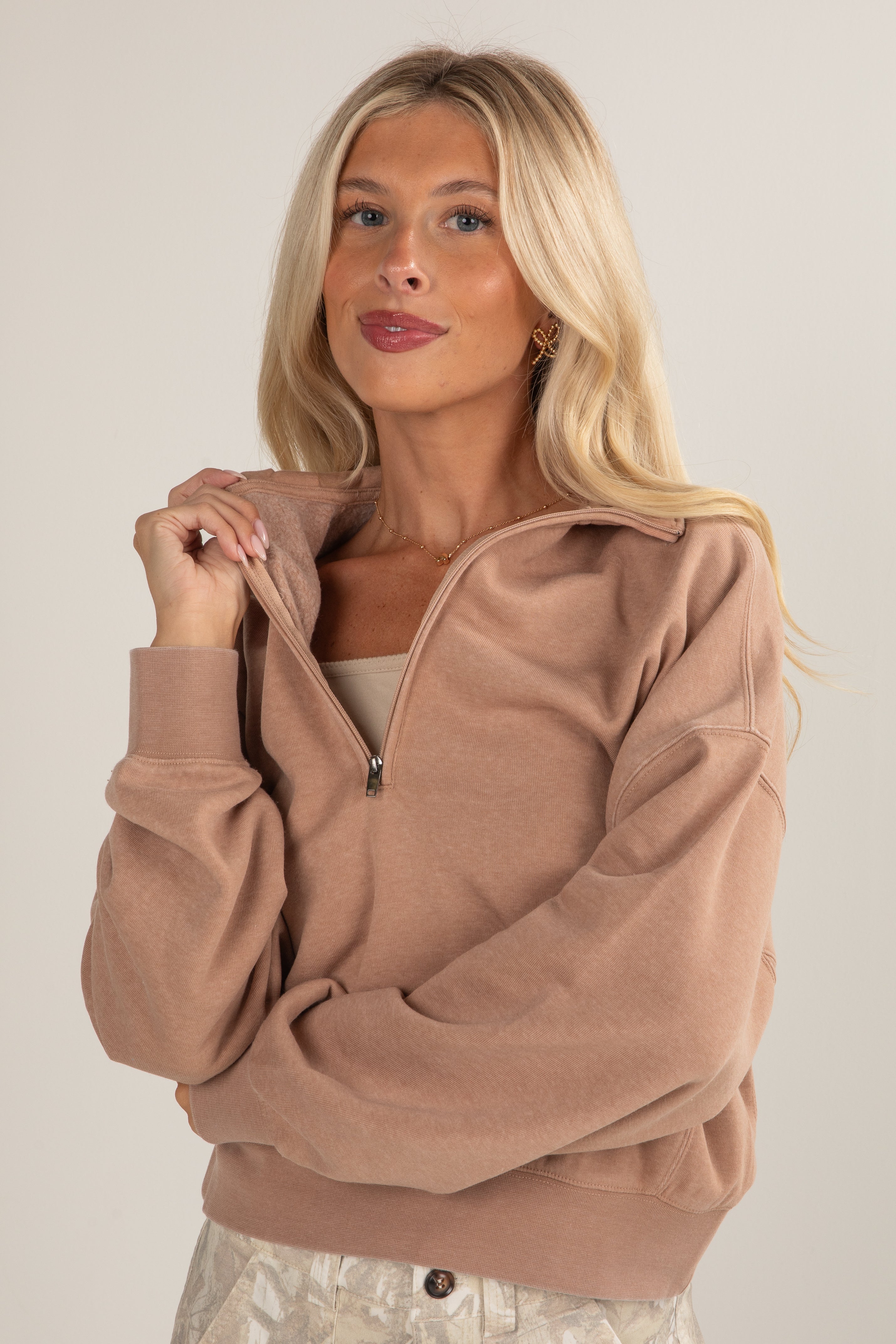 Woman wearing a brown zip-up sweatshirt against a plain background