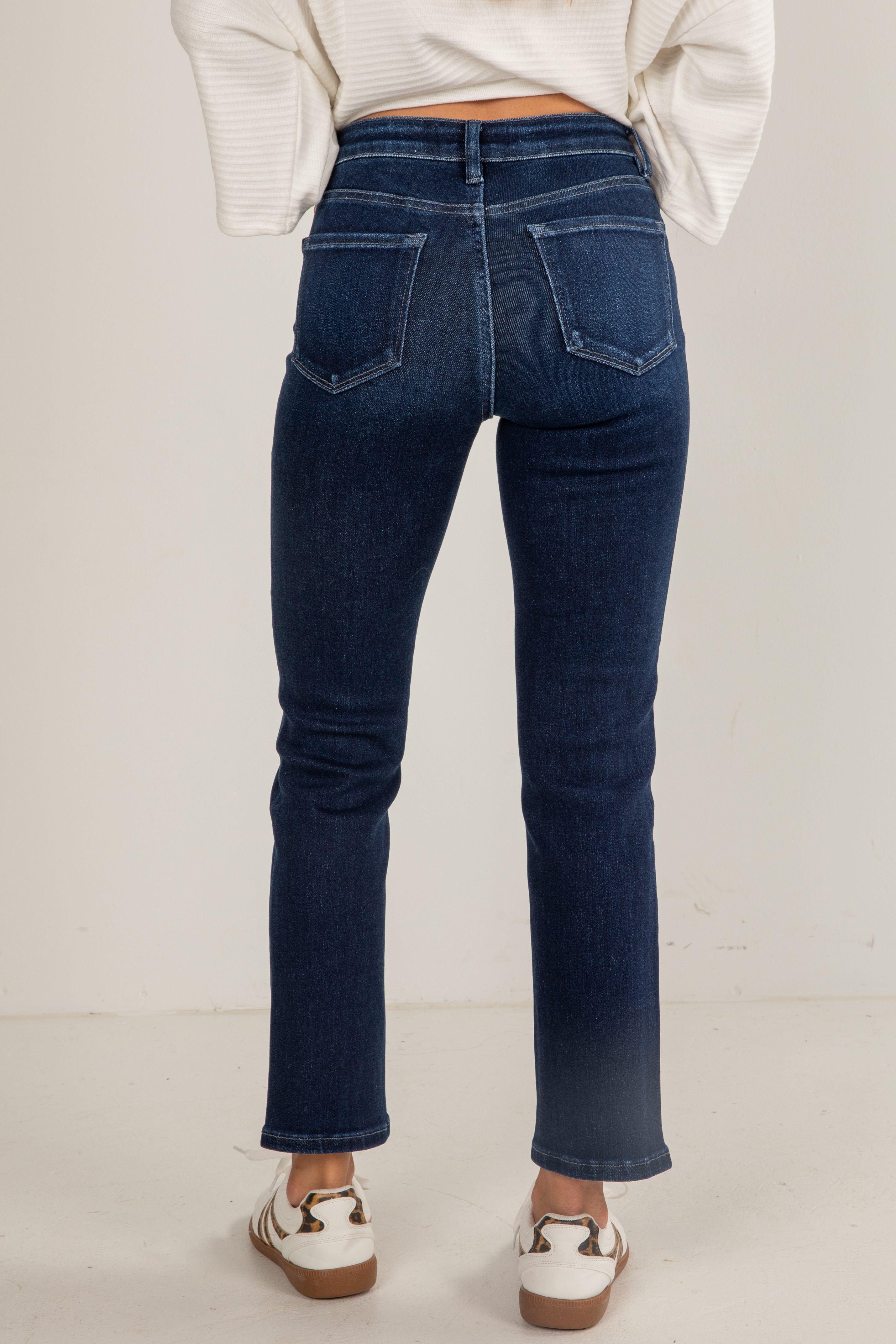 Person wearing dark blue jeans on a plain background