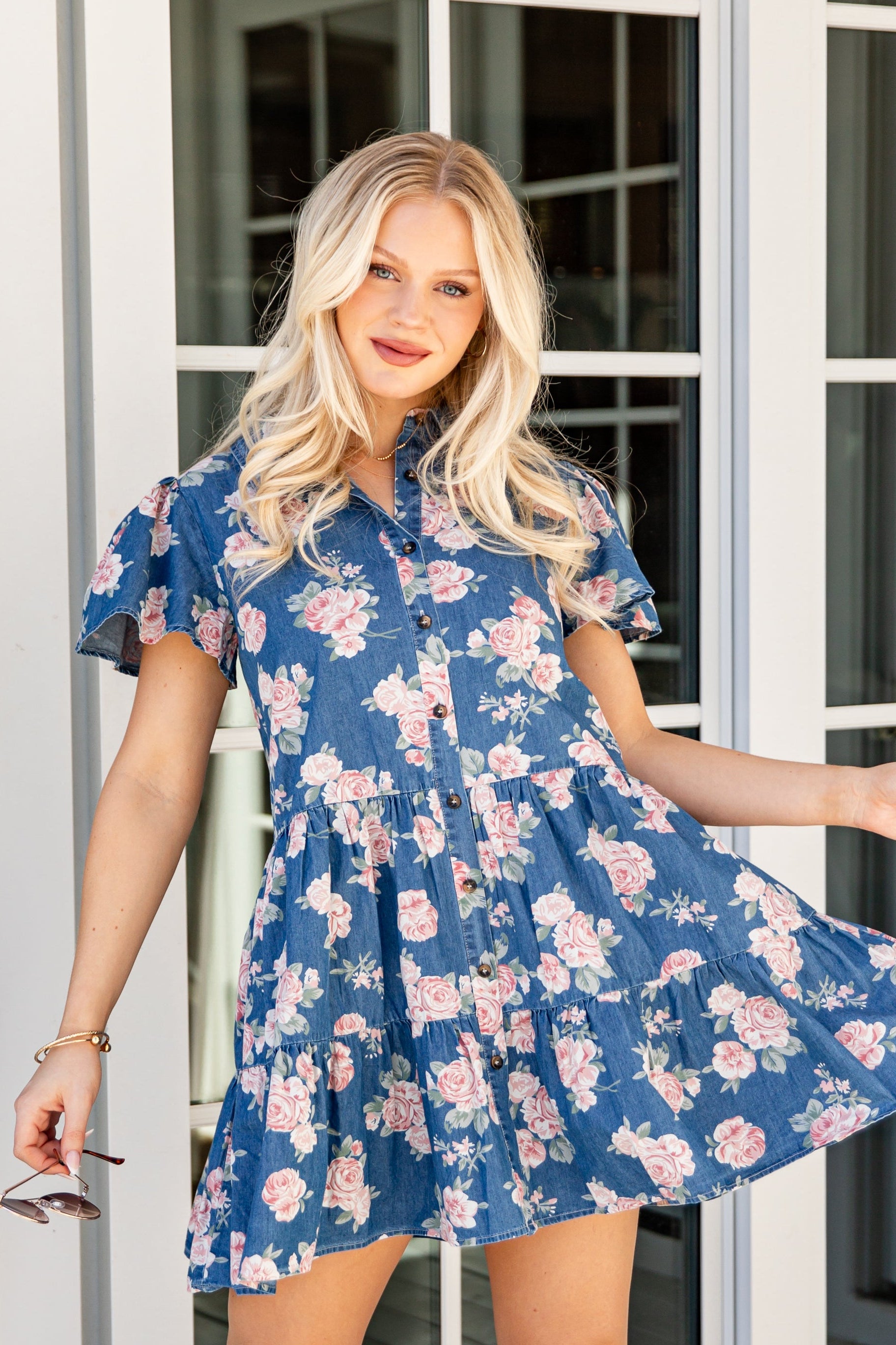 Woman in a blue floral dress standing on a wooden deck.
