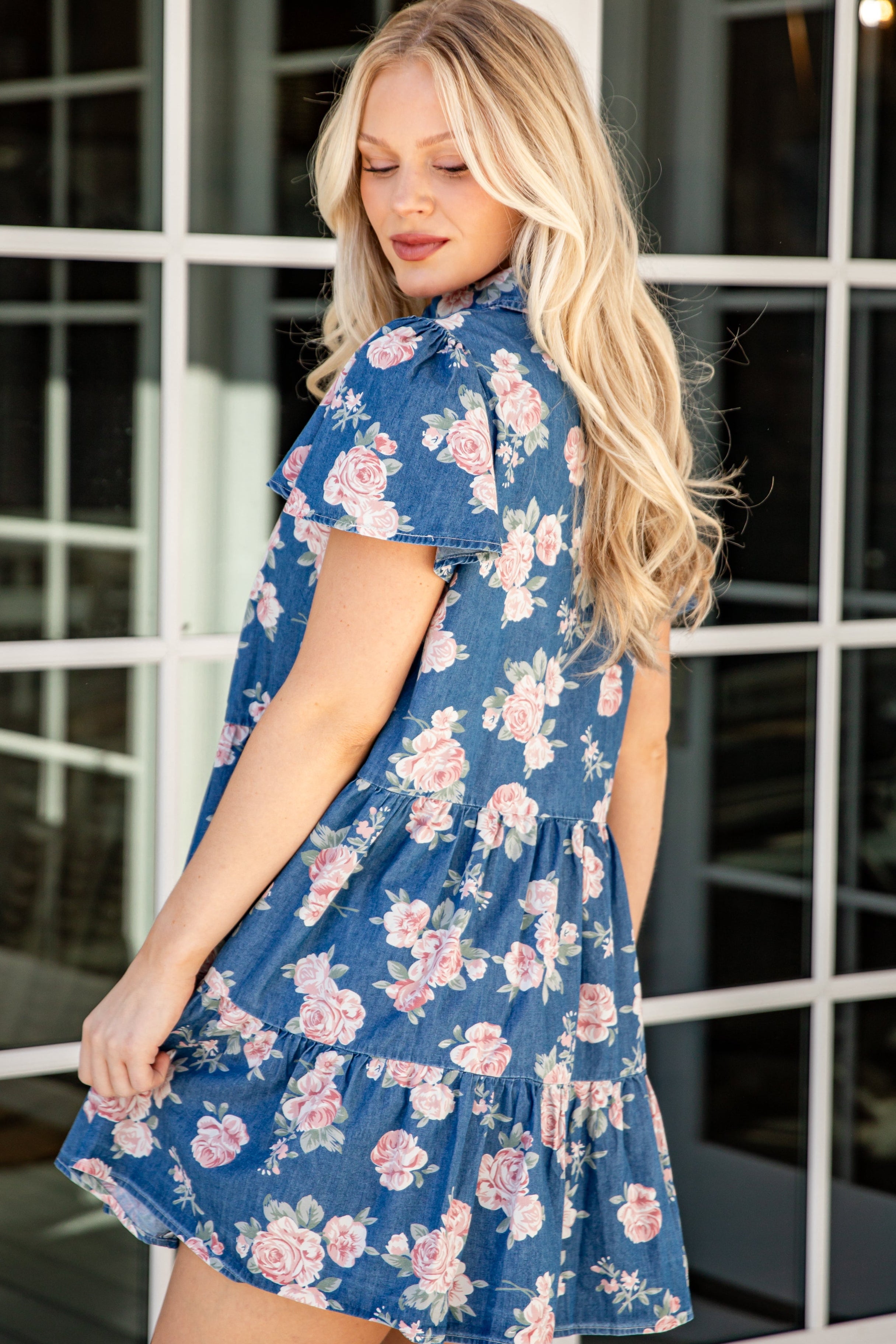 Woman wearing a blue floral dress standing in front of a glass door.