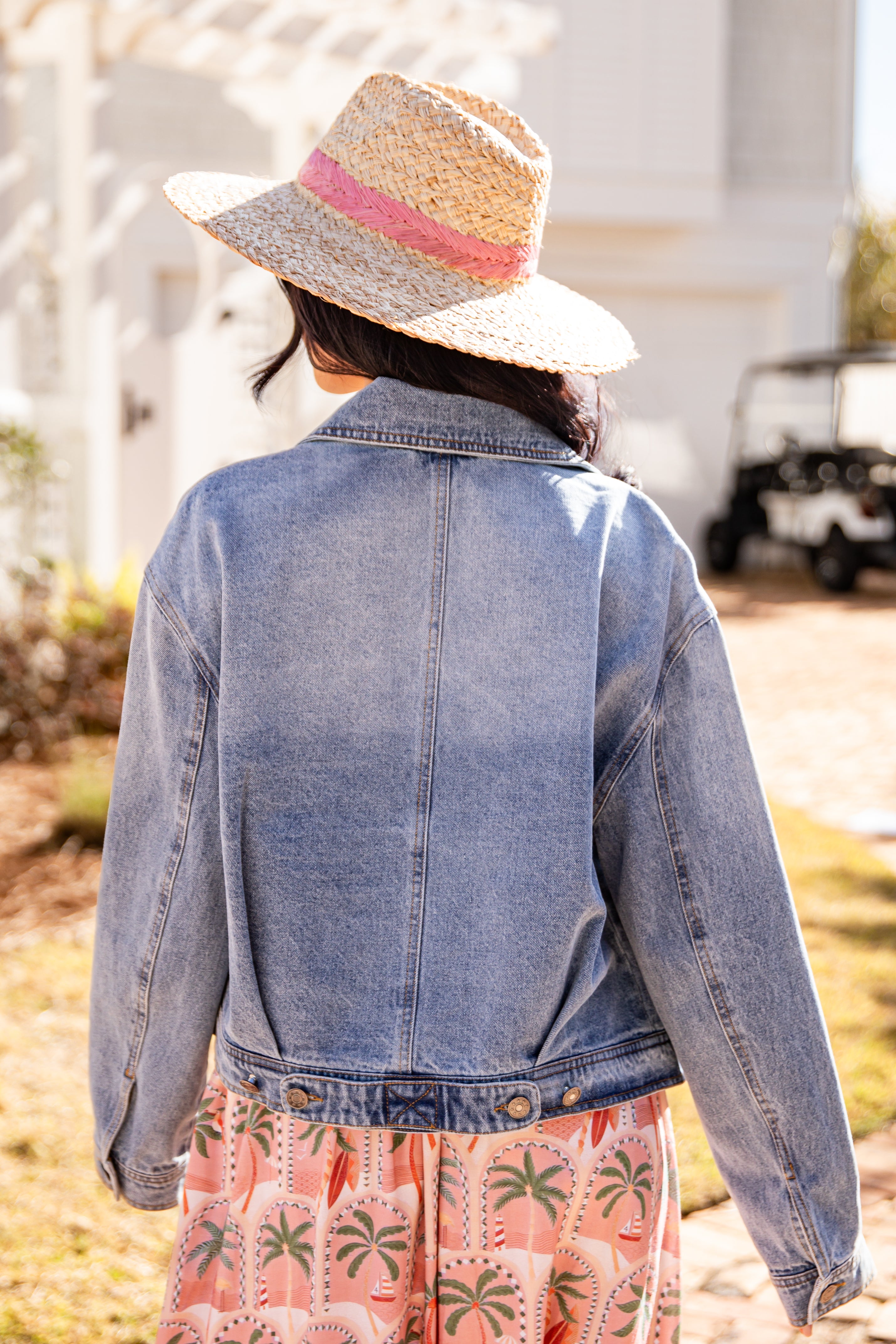 Person wearing a denim jacket and straw hat with a blurred background