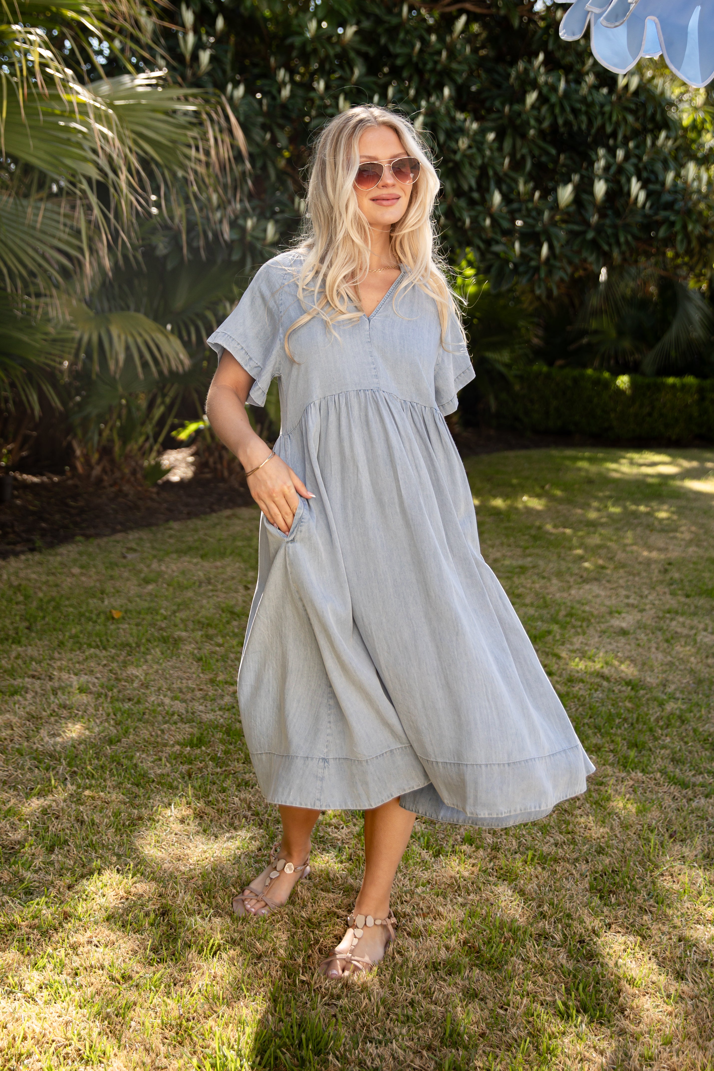 Woman in a light blue dress standing outdoors with greenery in the background