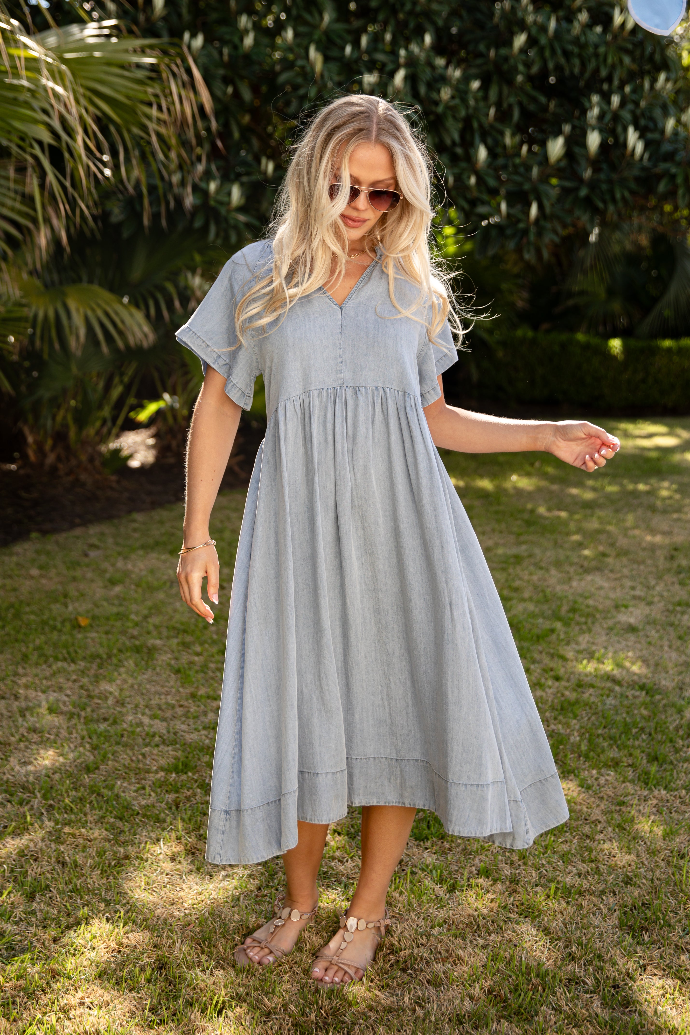 Woman wearing a light blue dress standing outdoors on grass with trees in the background