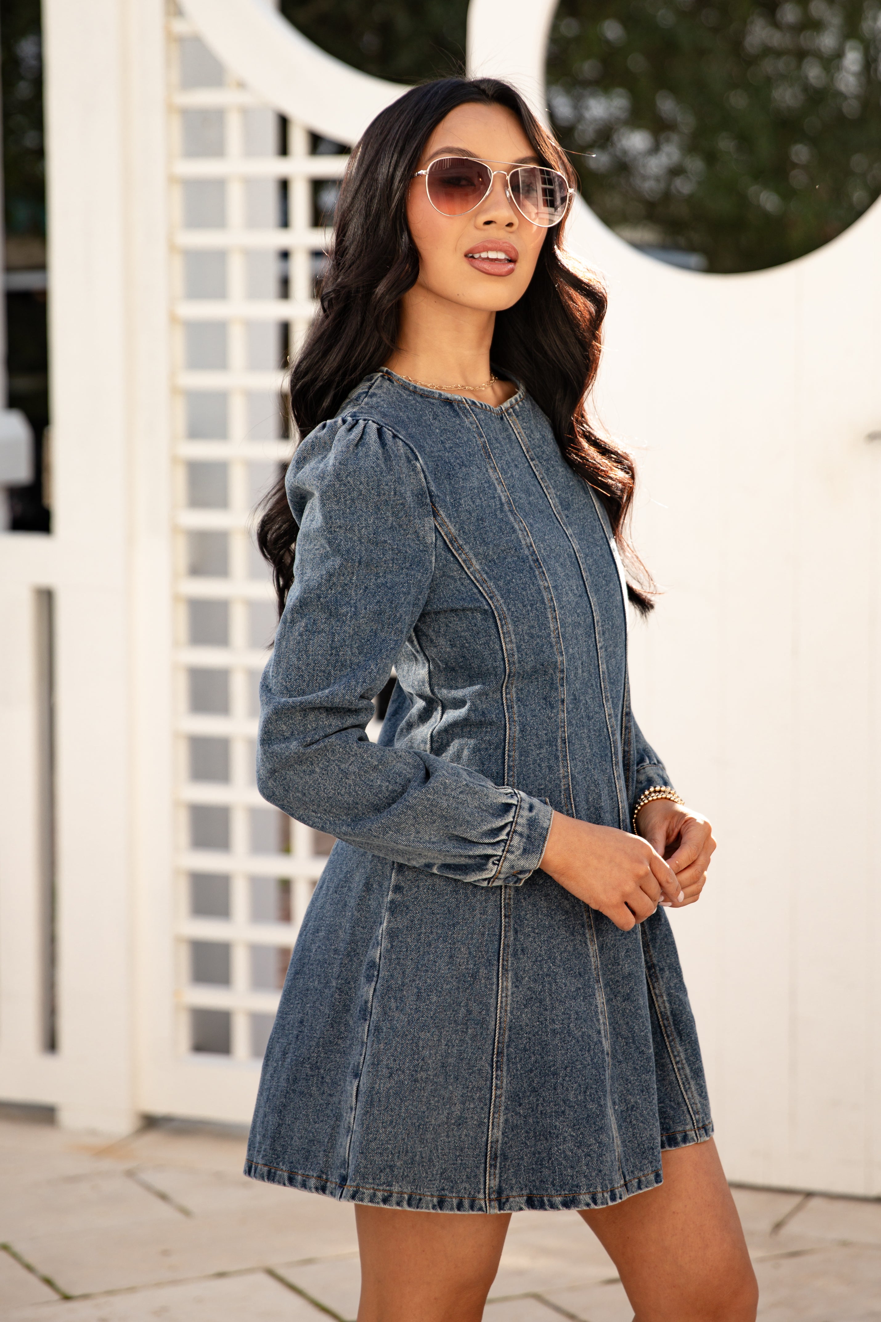 Woman wearing a denim dress with sunglasses outdoors.