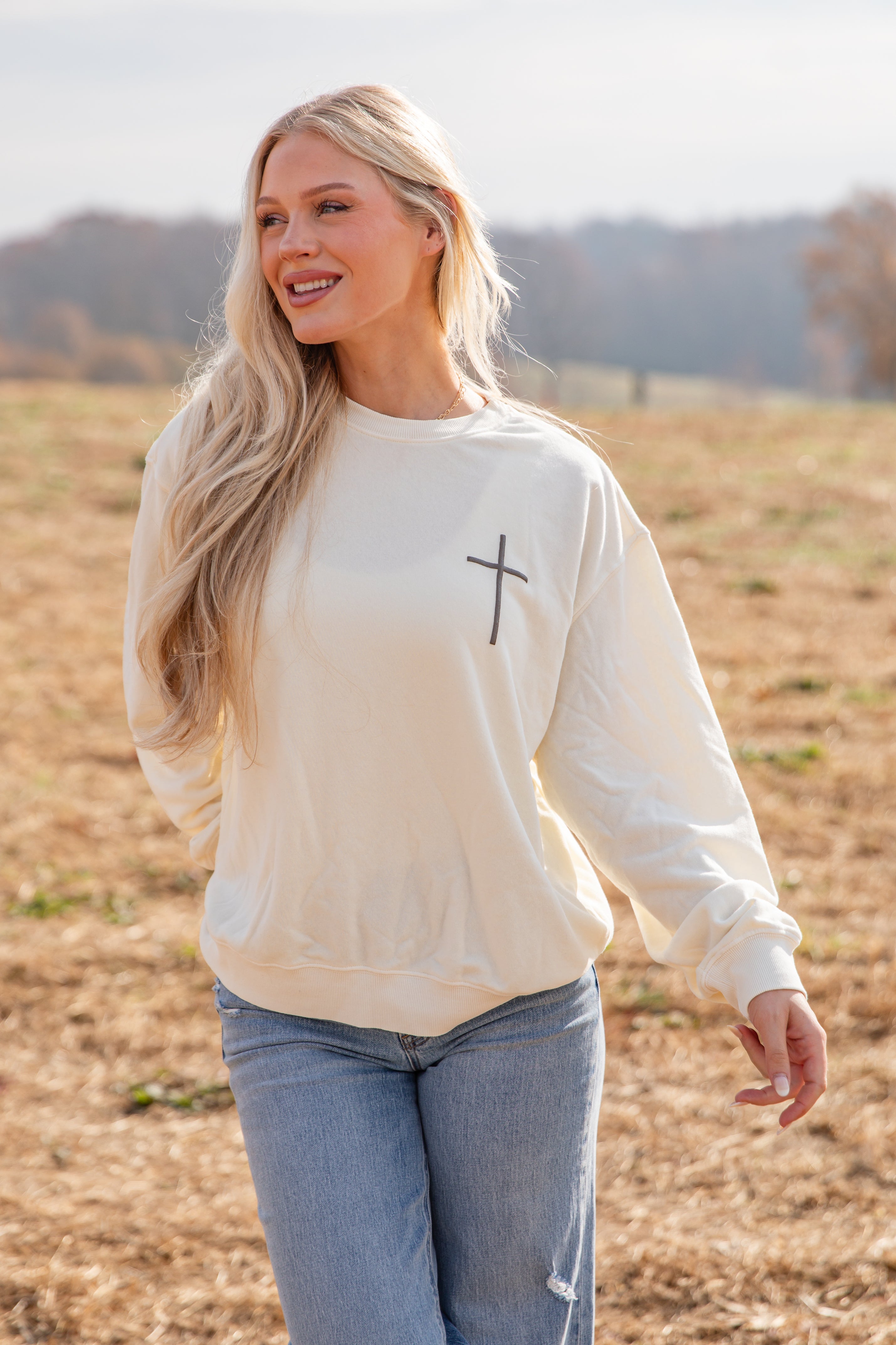 Woman wearing a beige sweatshirt with a cross design in a field