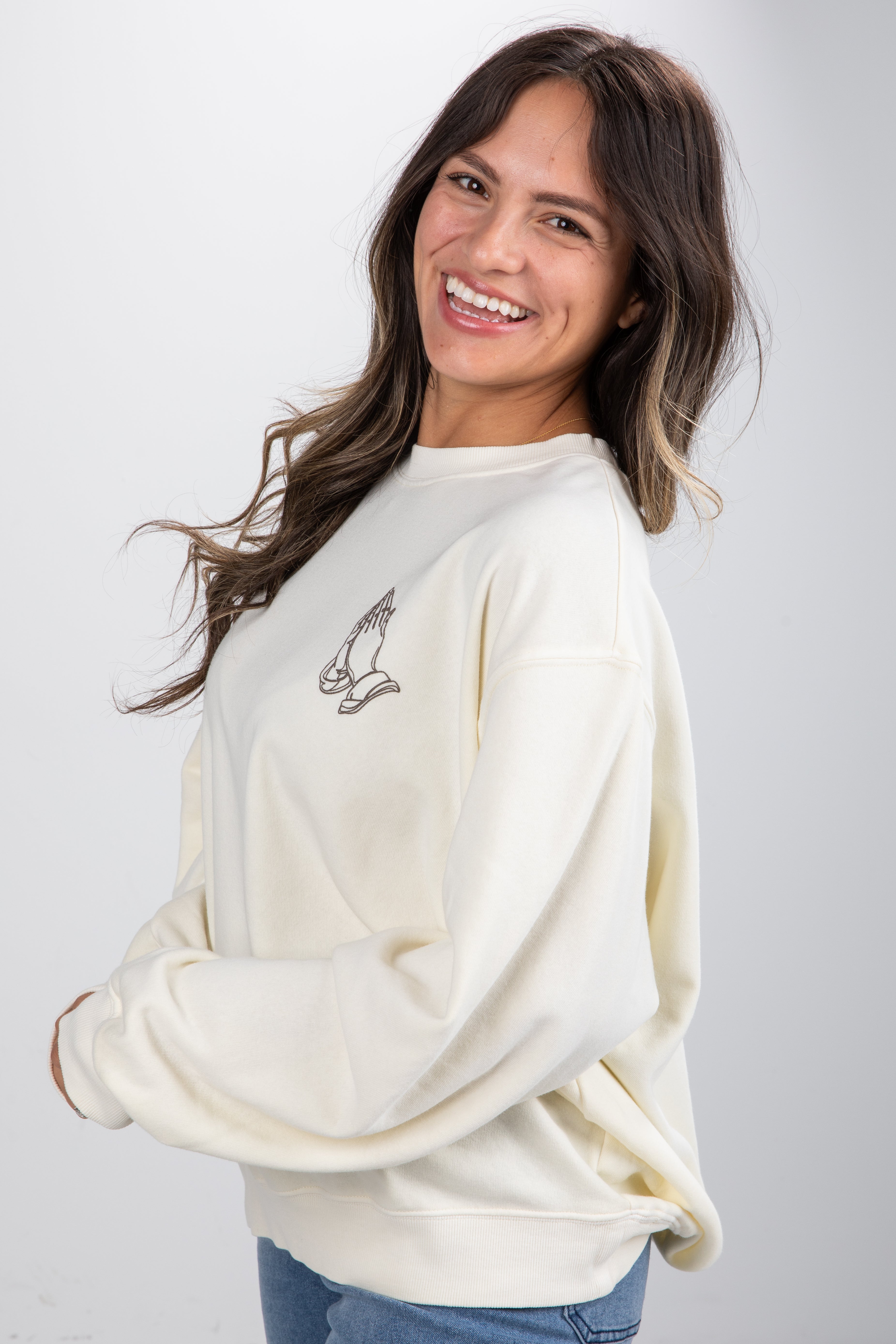 Woman wearing a cream-colored sweatshirt with a logo on a plain background