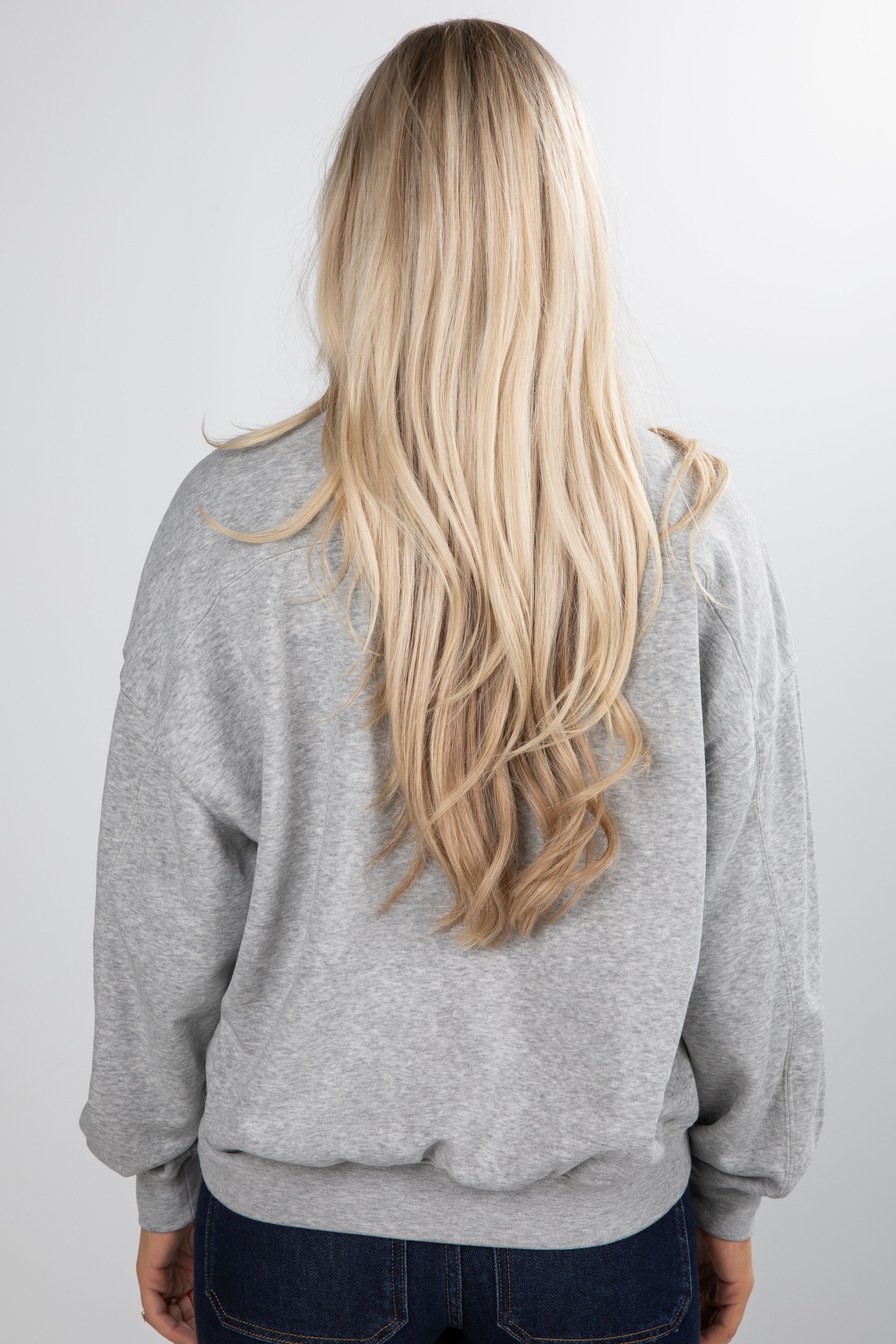 Person wearing a gray hoodie with long blonde hair, standing against a plain background