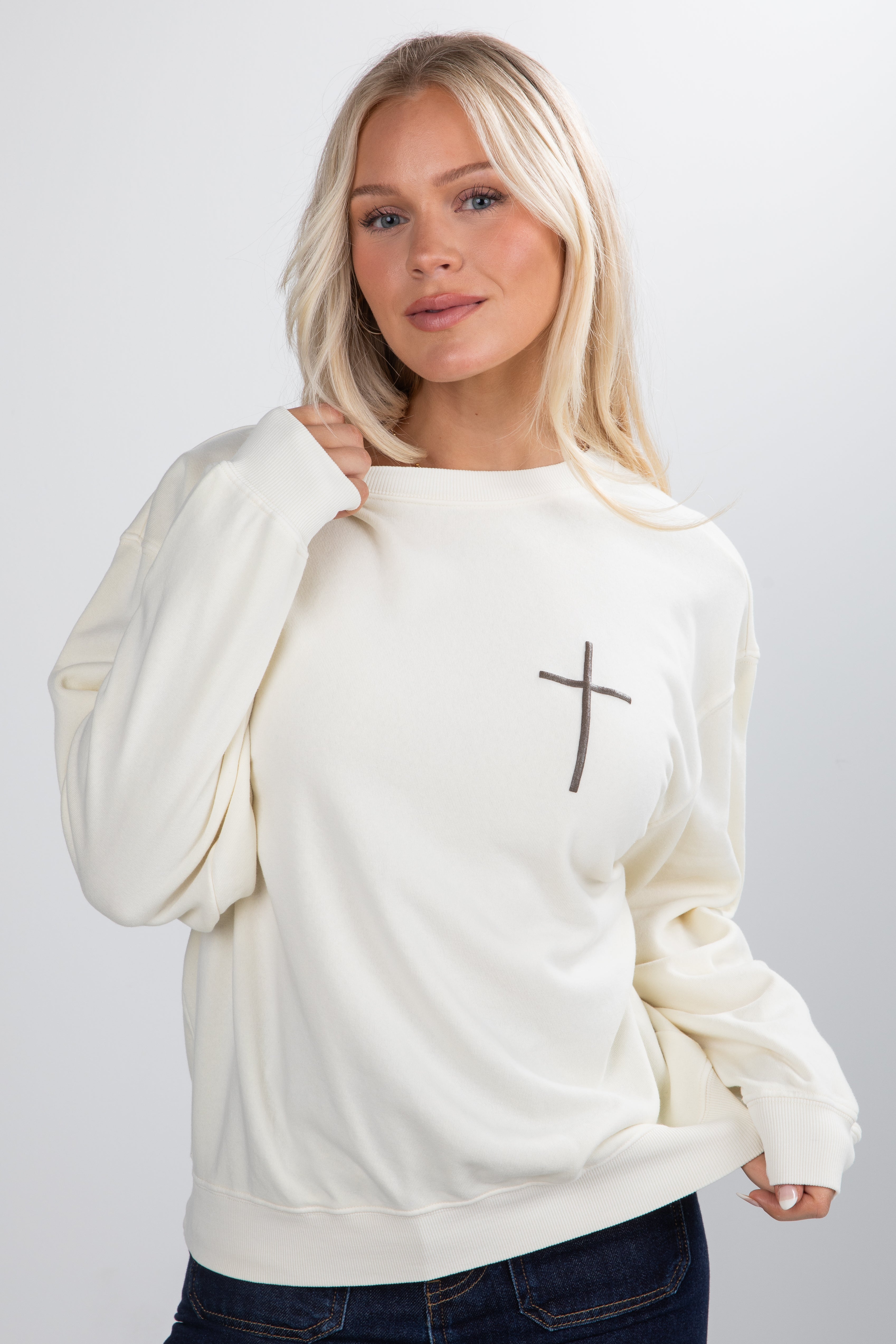 Woman wearing a white sweatshirt with a cross design on a plain background