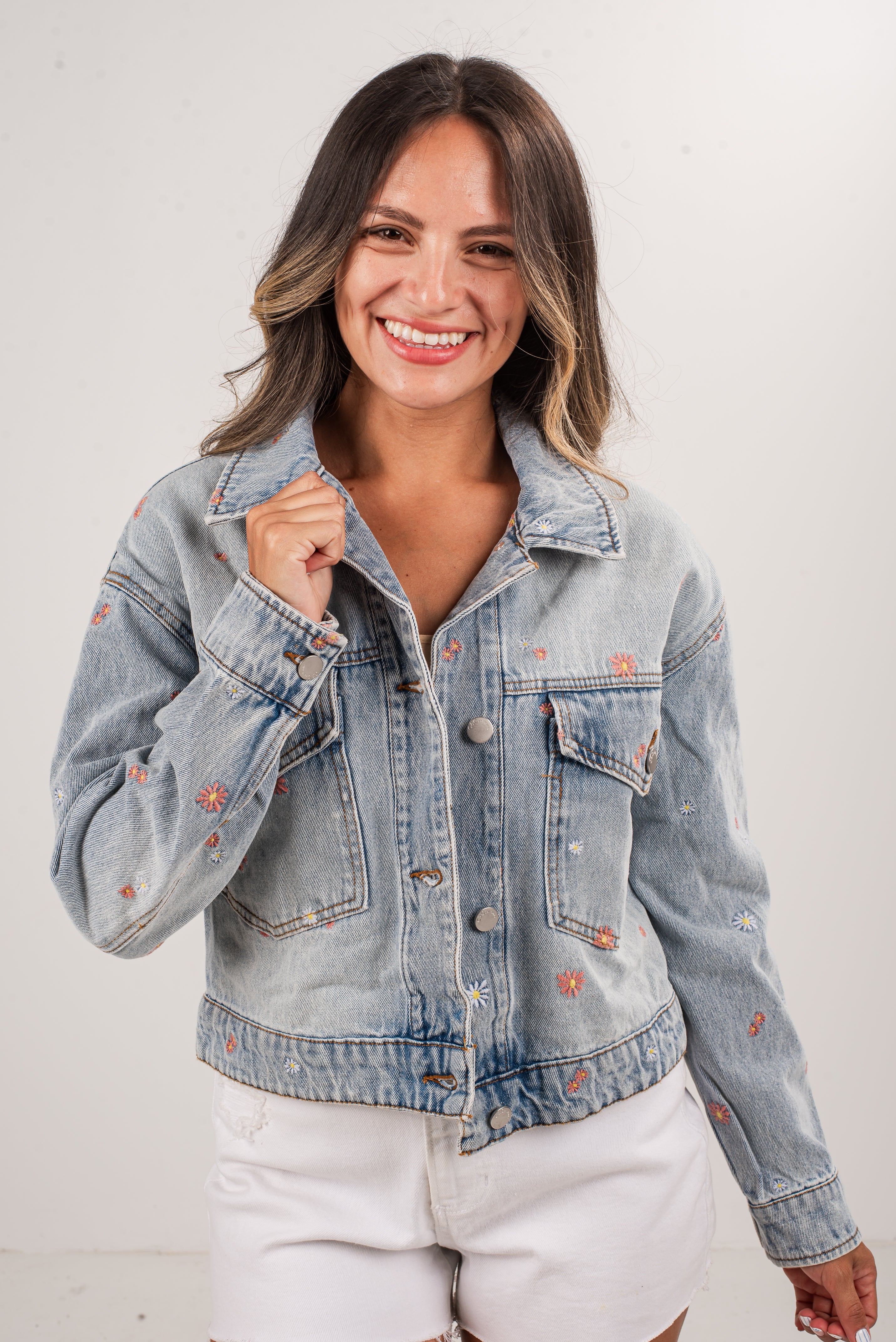 Woman wearing a light blue denim jacket with floral embroidery on a white background