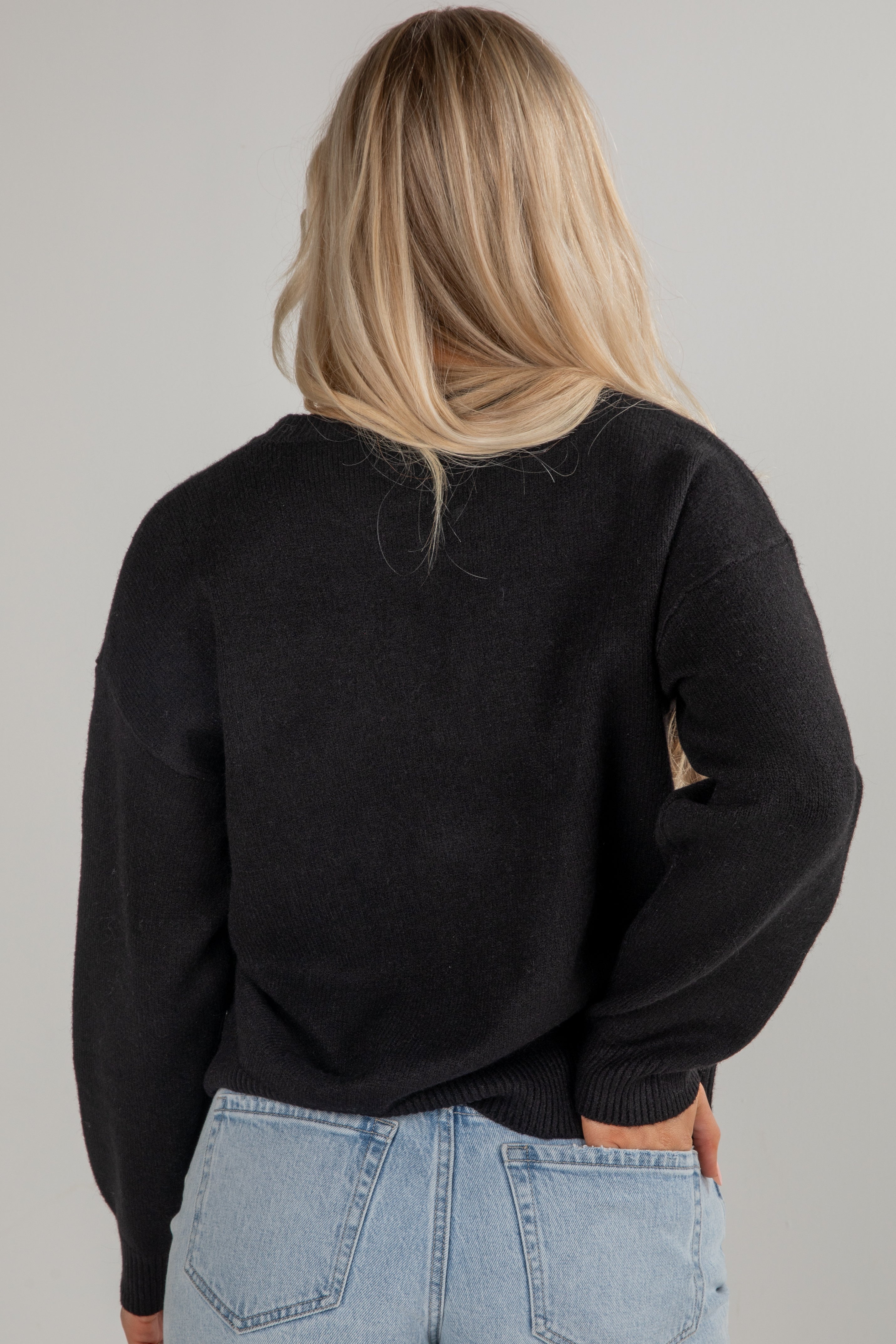 Person wearing a black sweater and light blue jeans on a gray background