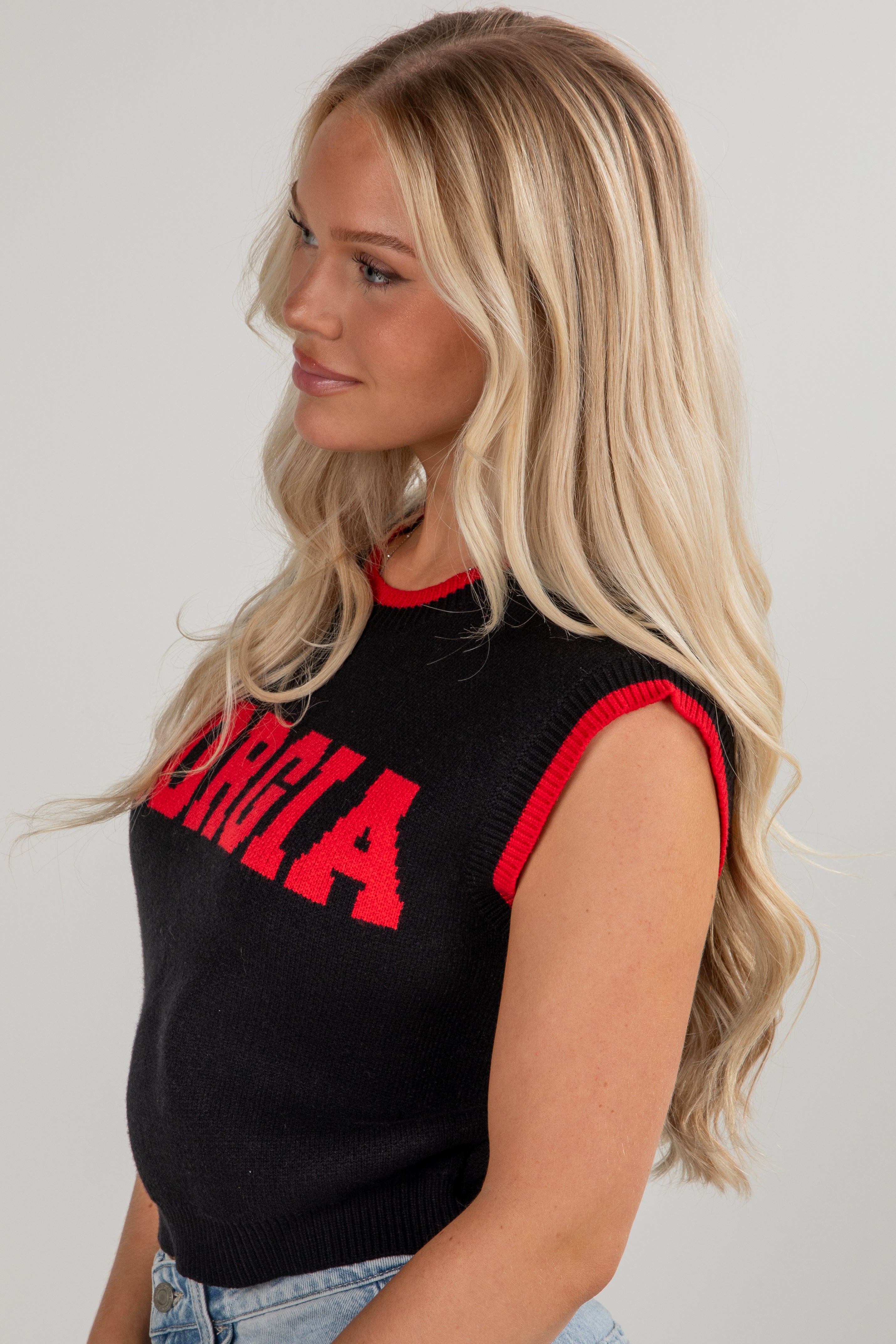 Woman wearing a black sleeveless top with red lettering against a plain background