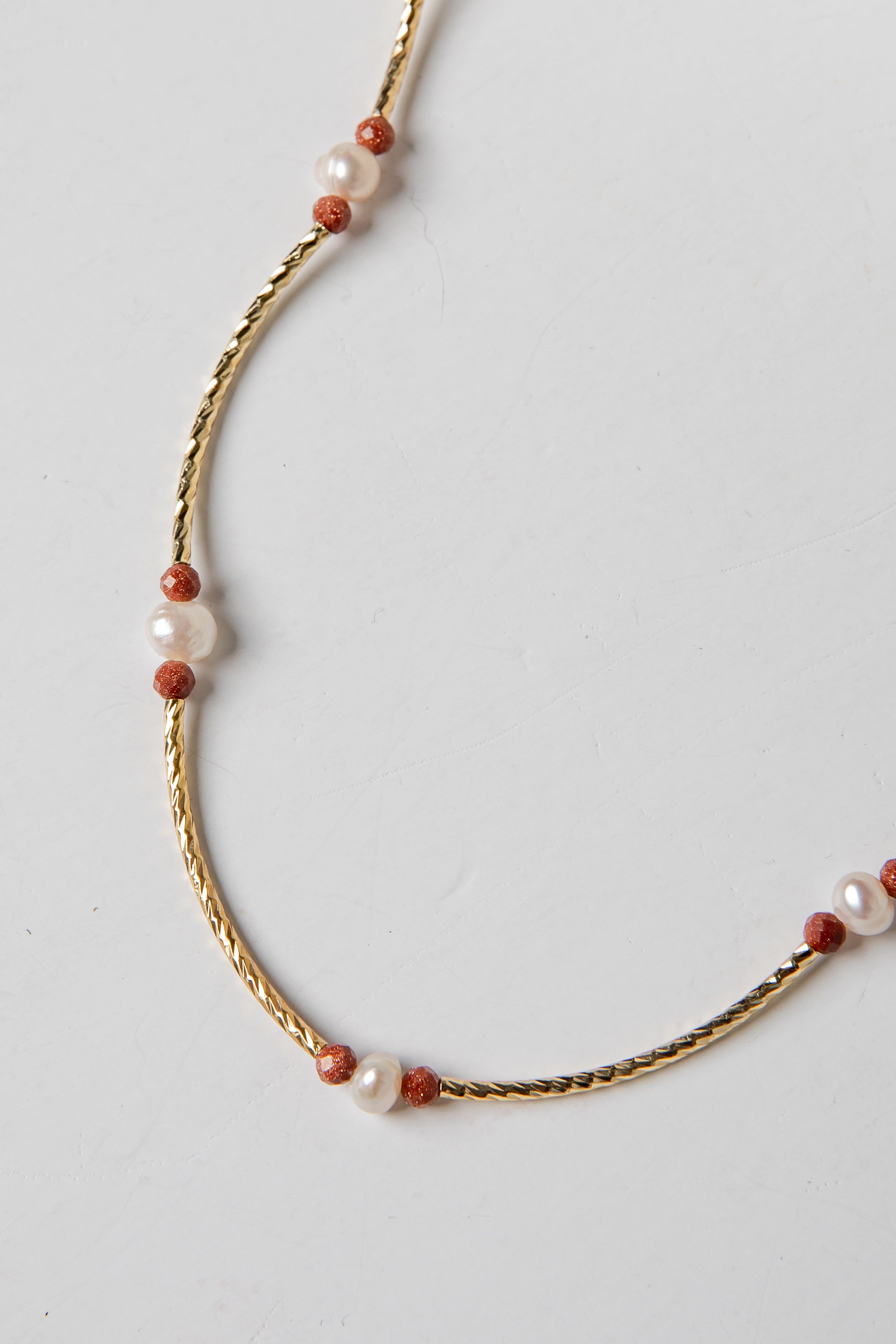 Necklace with gold chain and red and white beads on a light gray background