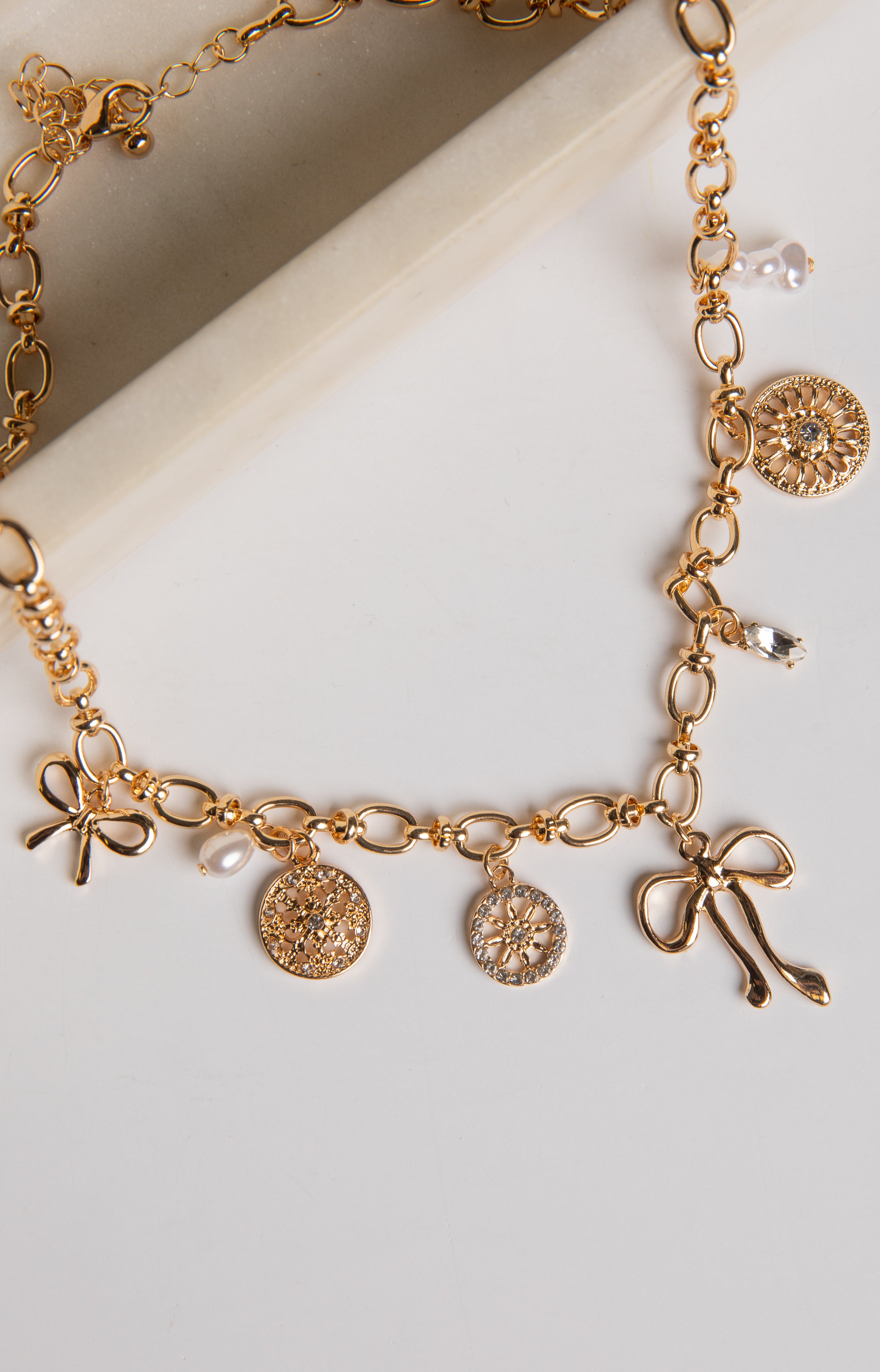 Gold necklace with bow and coin charms on a white background