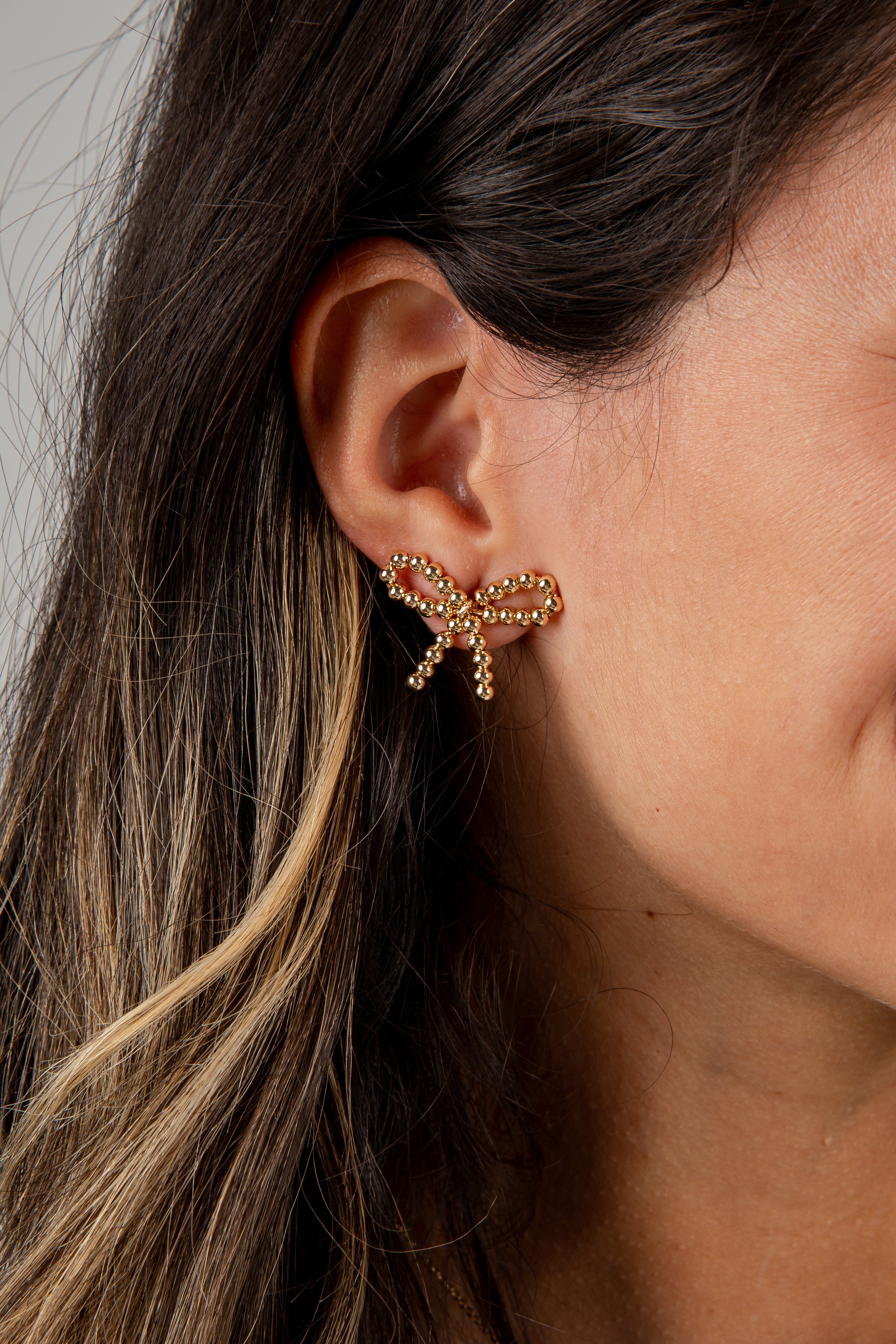 Close-up of an ear wearing a gold bow-shaped earring with a blurred background