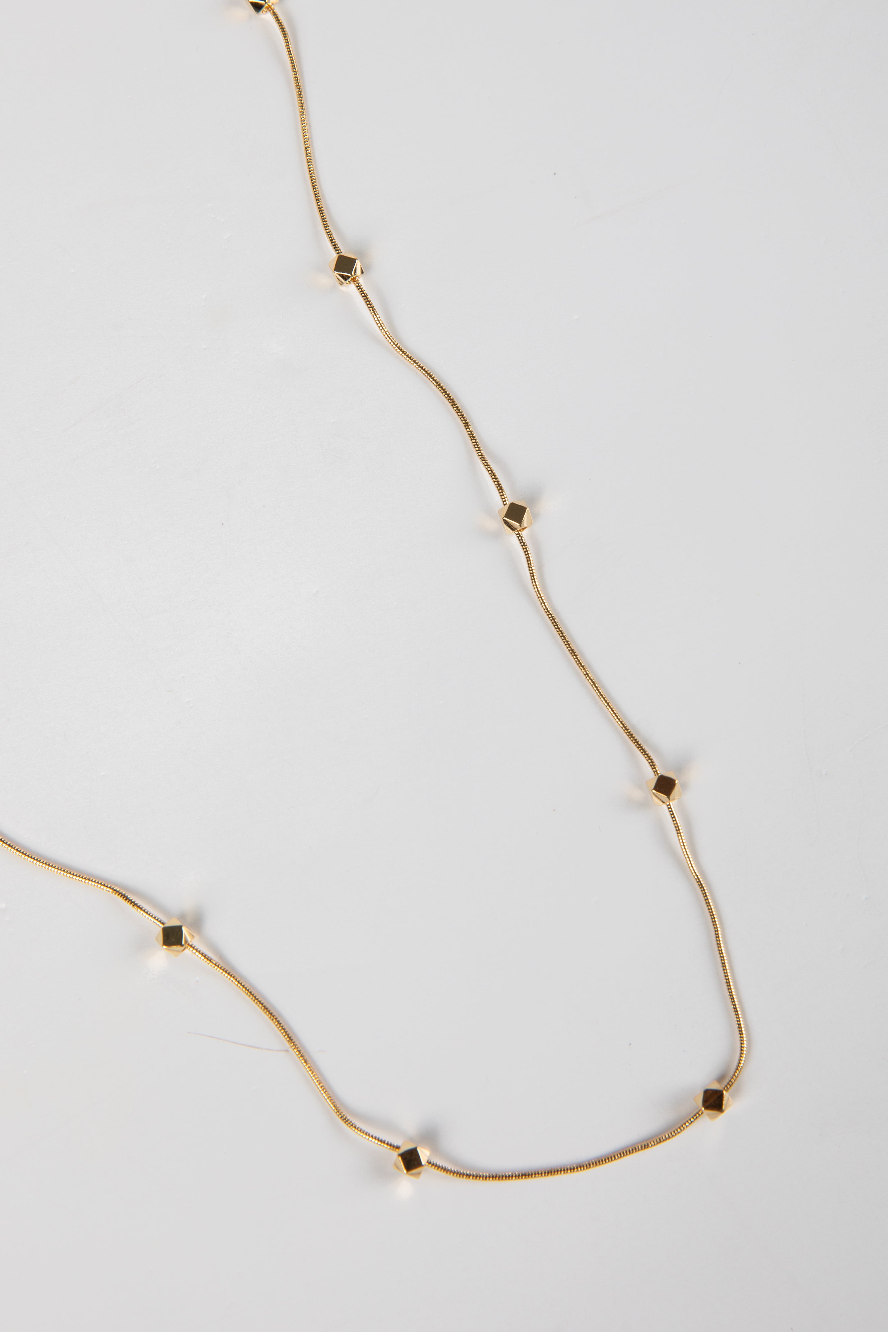 Gold necklace with small square pendants on a light gray background