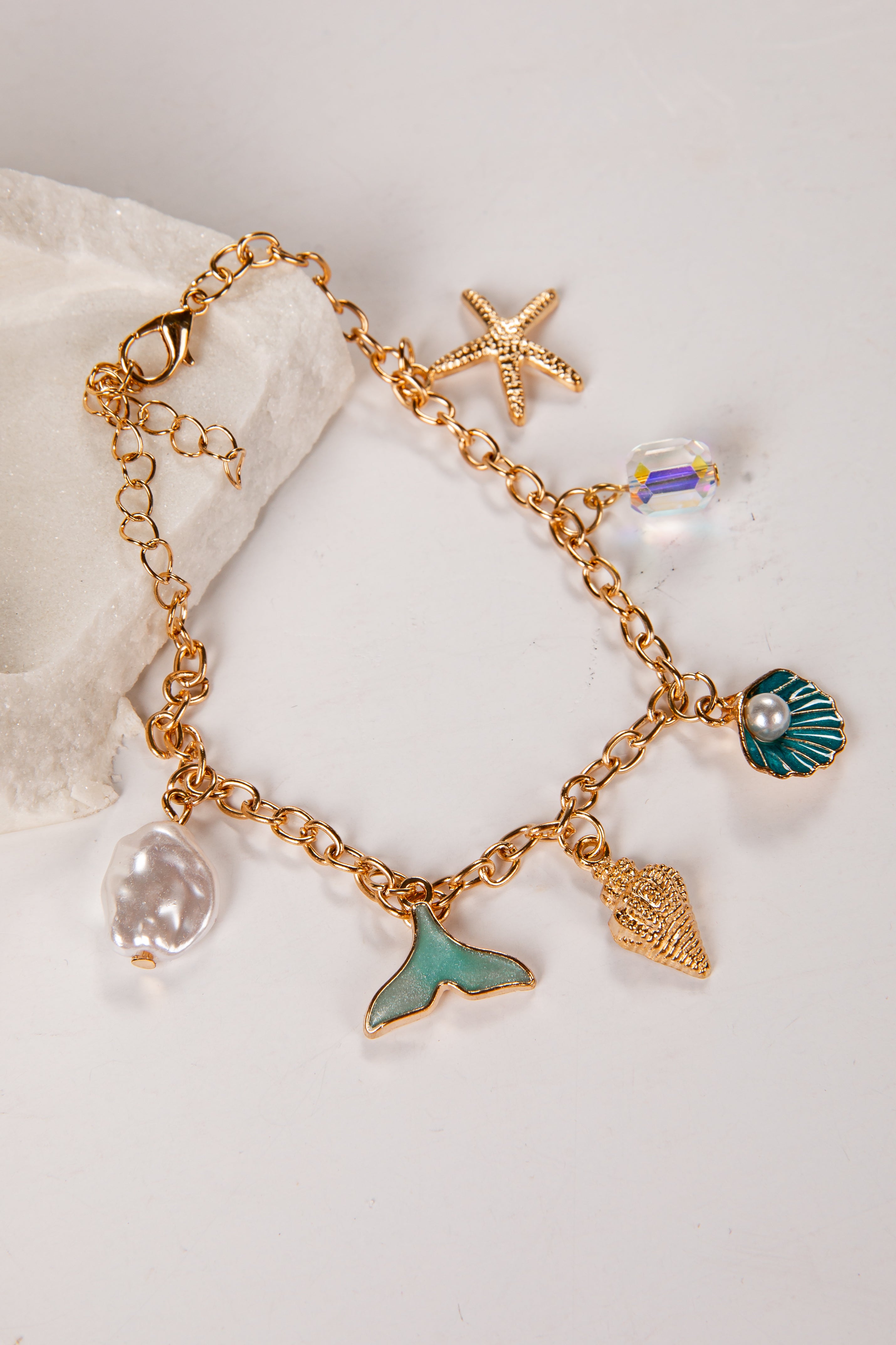 Gold bracelet with various charms including a mermaid tail, starfish, and shell on a light background.