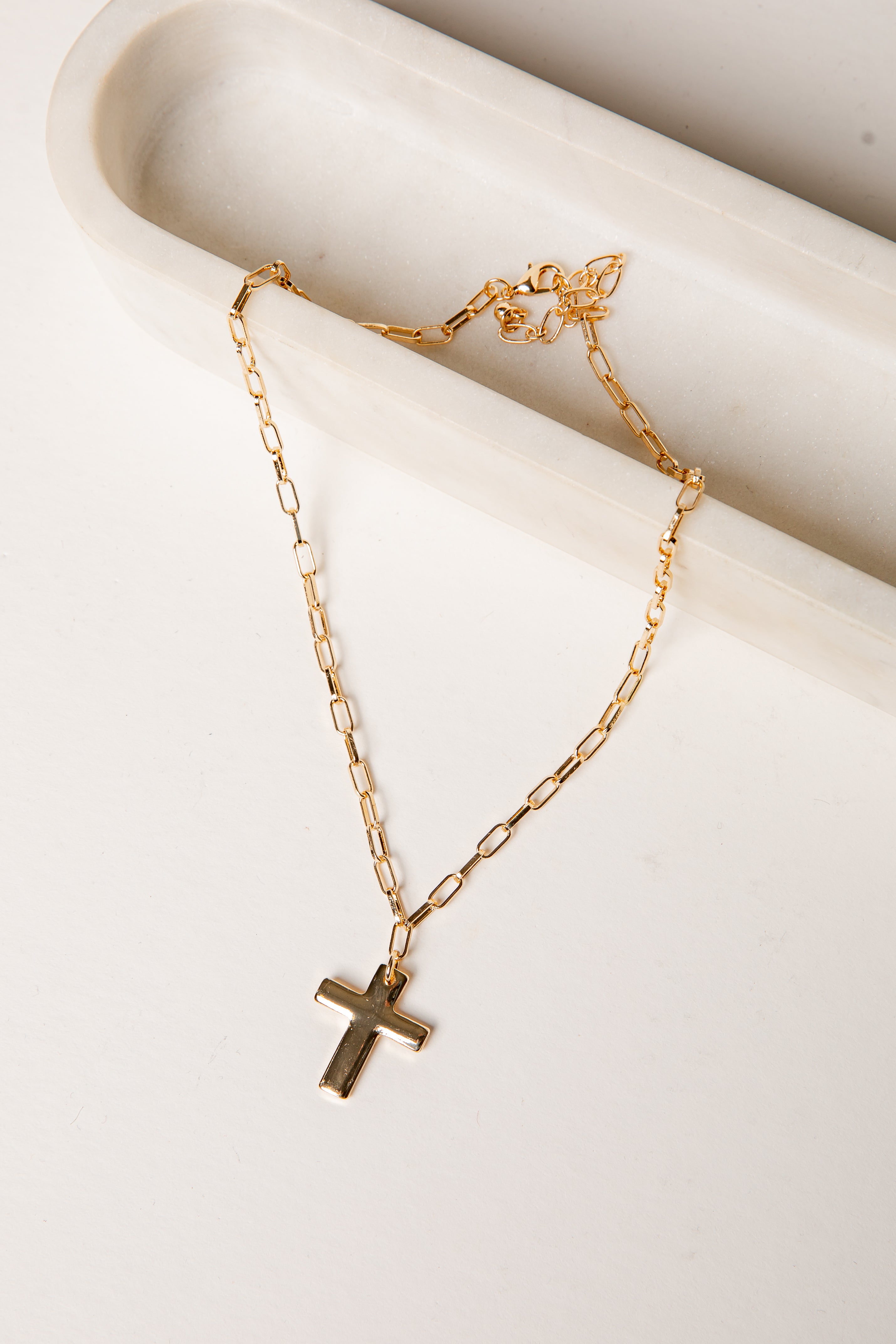 Gold necklace with a cross pendant on a white surface