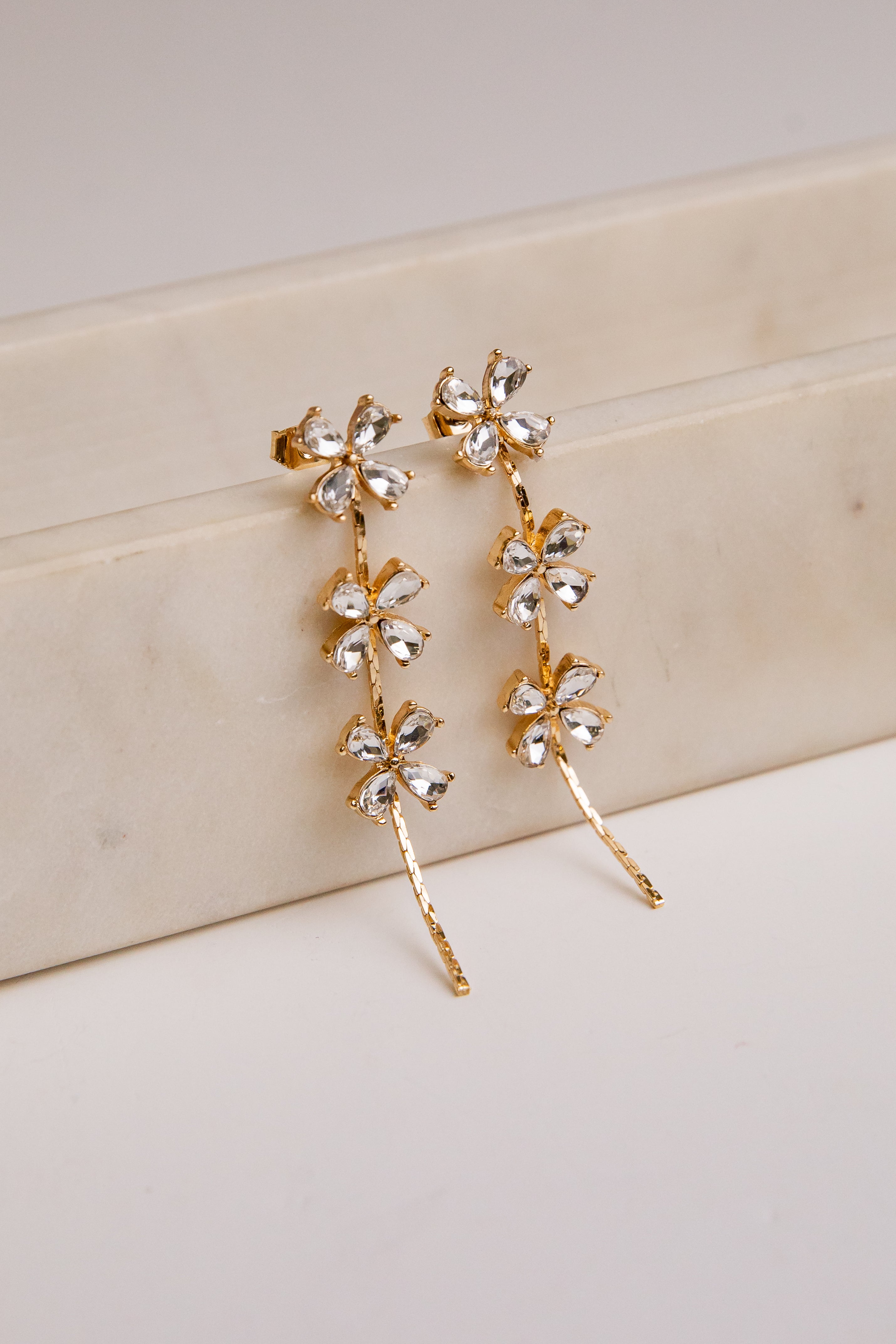 Gold floral earrings on a light wooden surface