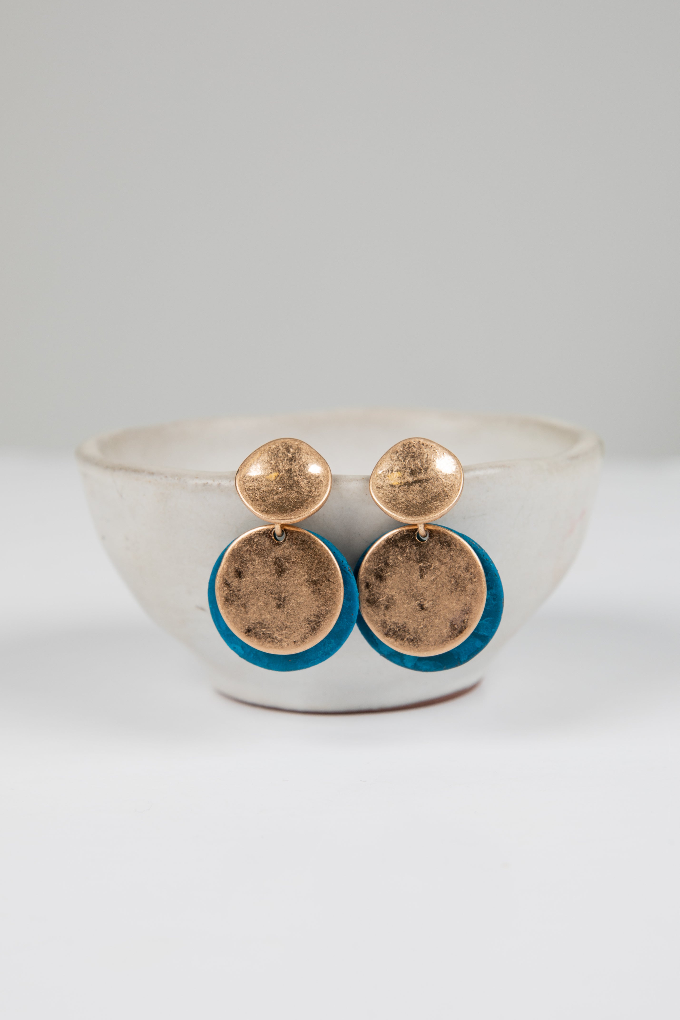 Gold earrings with blue accents on a white dish against a light gray background
