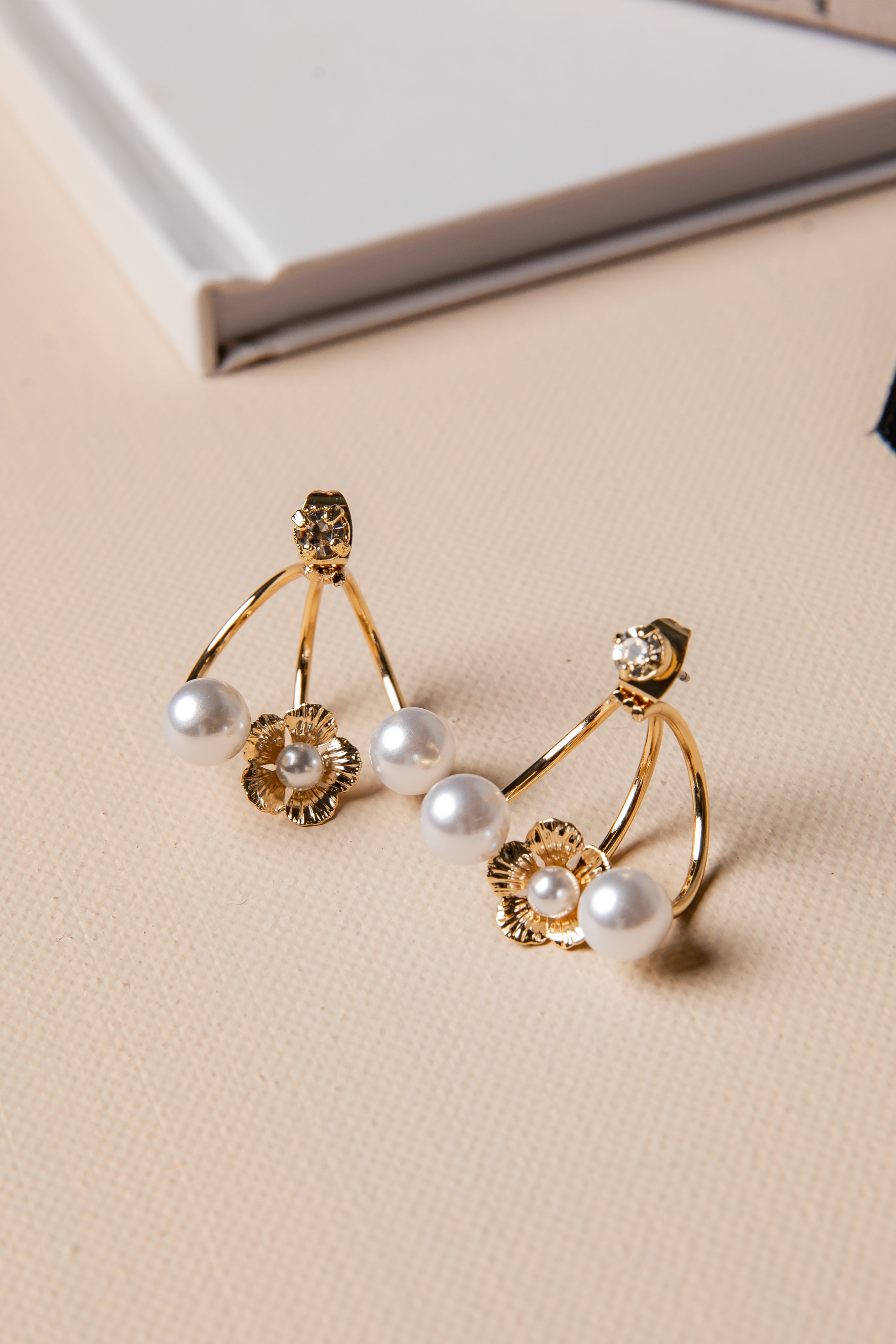 Gold earrings with pearls on a beige surface