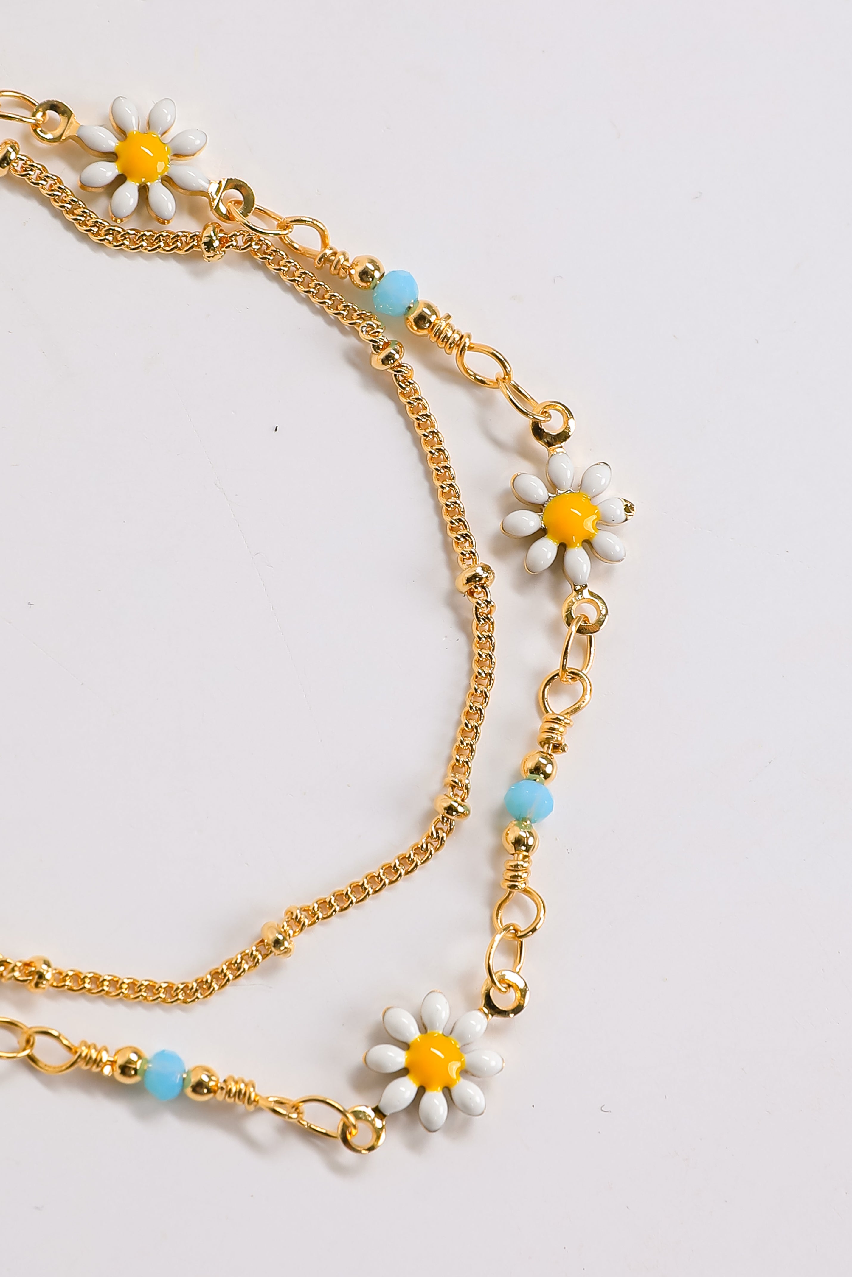 Gold chain necklace with daisy flower pendants on a light gray background