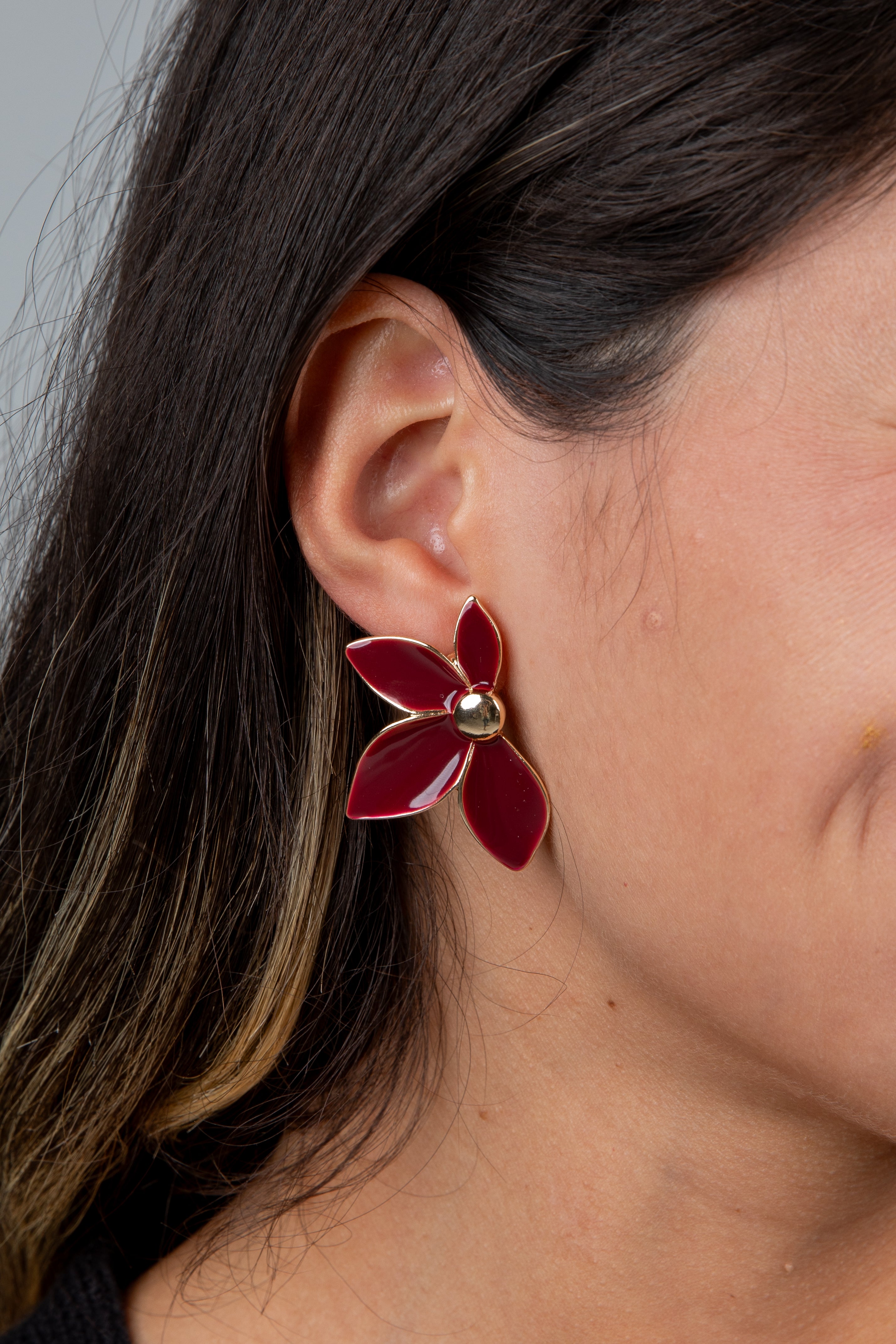 Close-up of a person wearing a red flower-shaped earring with a gold center.