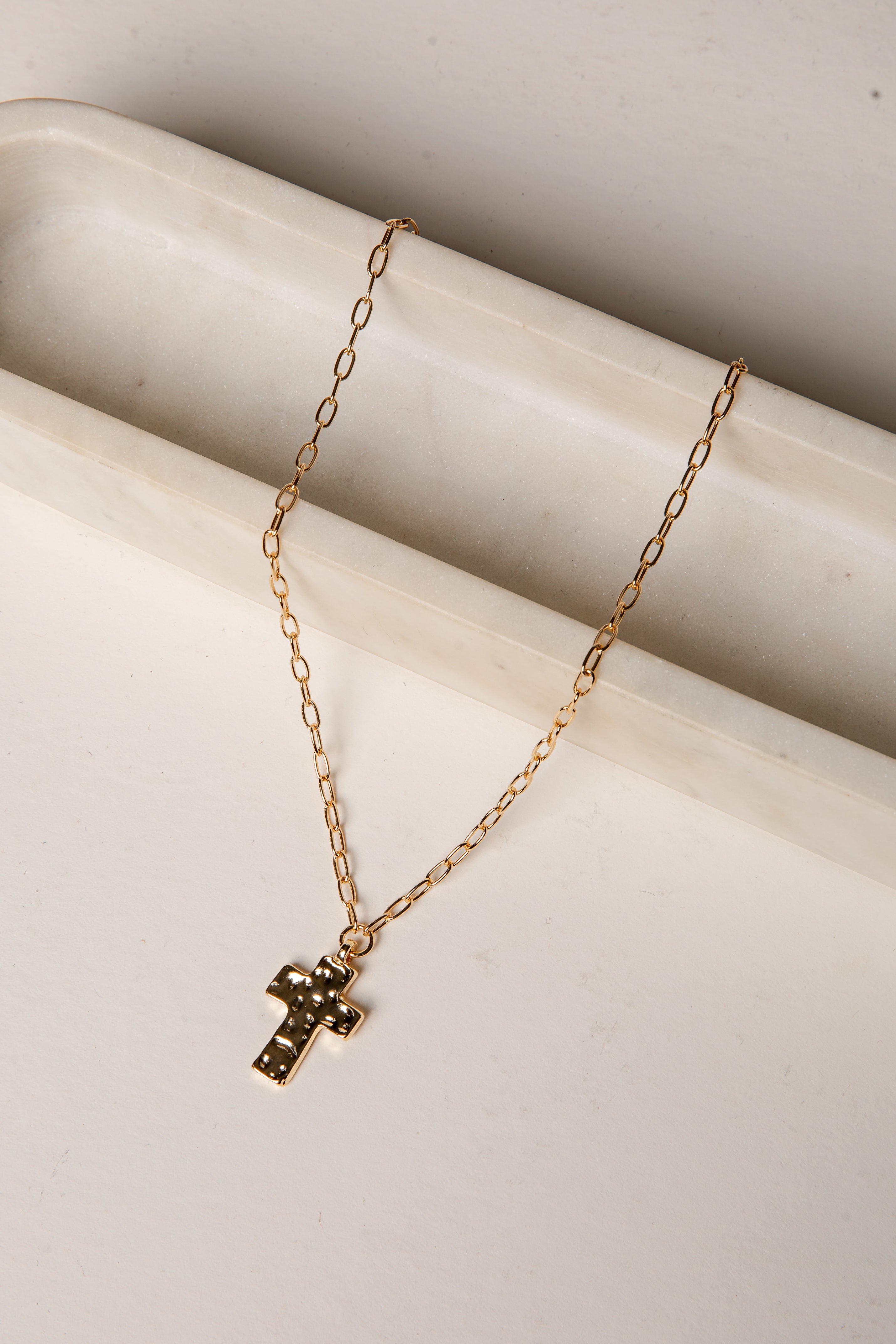 Gold necklace with a cross pendant on a light beige surface