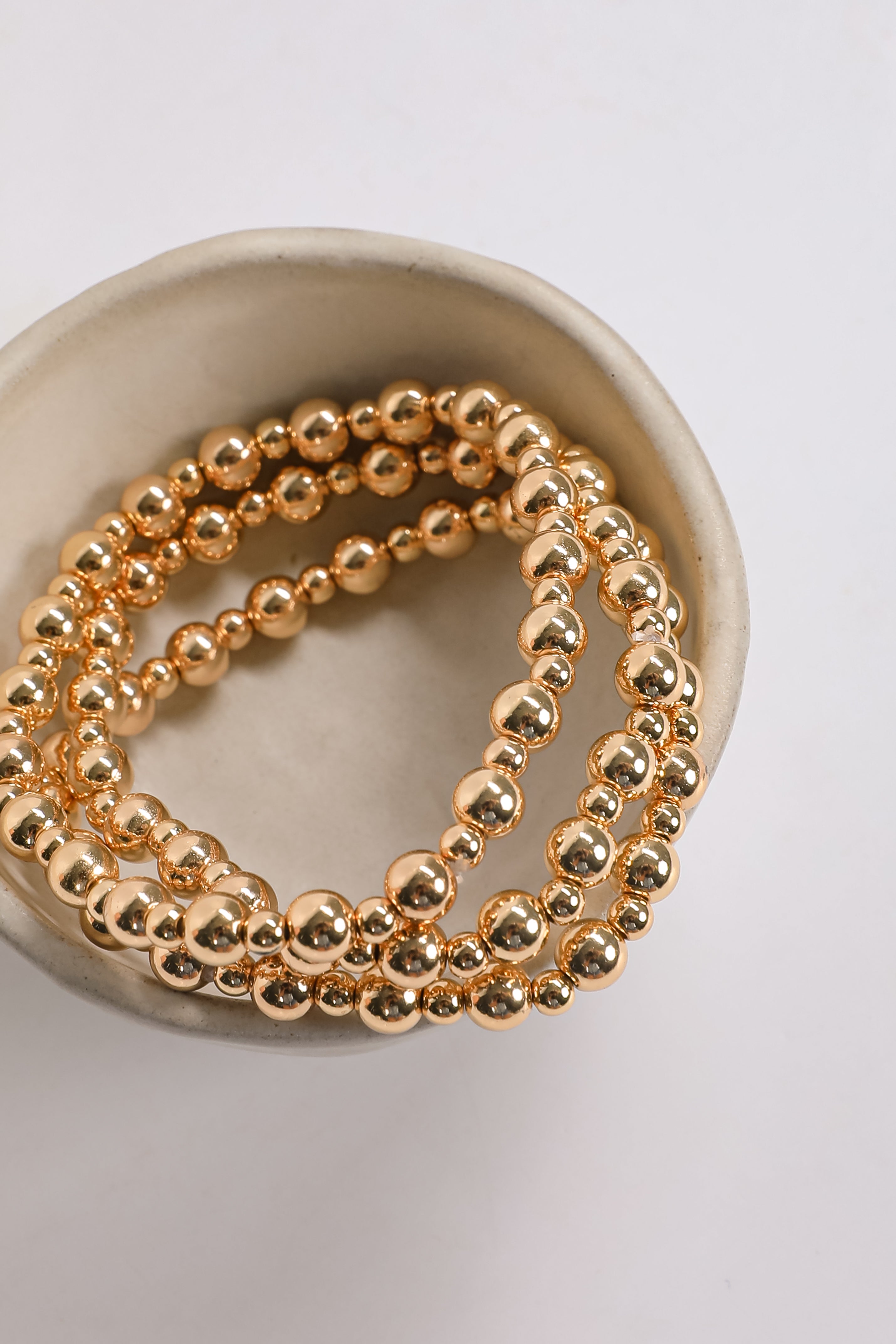Gold beaded bracelets on a white dish with a white background