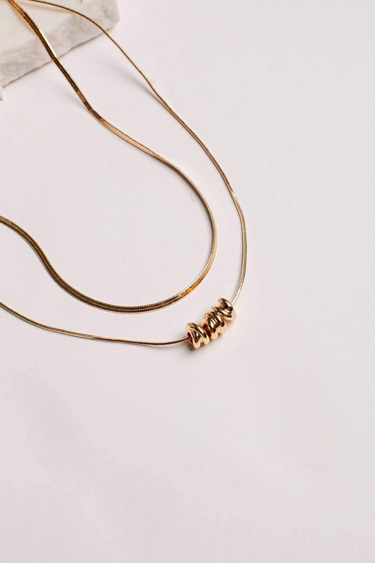 A gold-toned double-strand necklace featuring a textured, coiled bead pendant, displayed on a clean white surface.