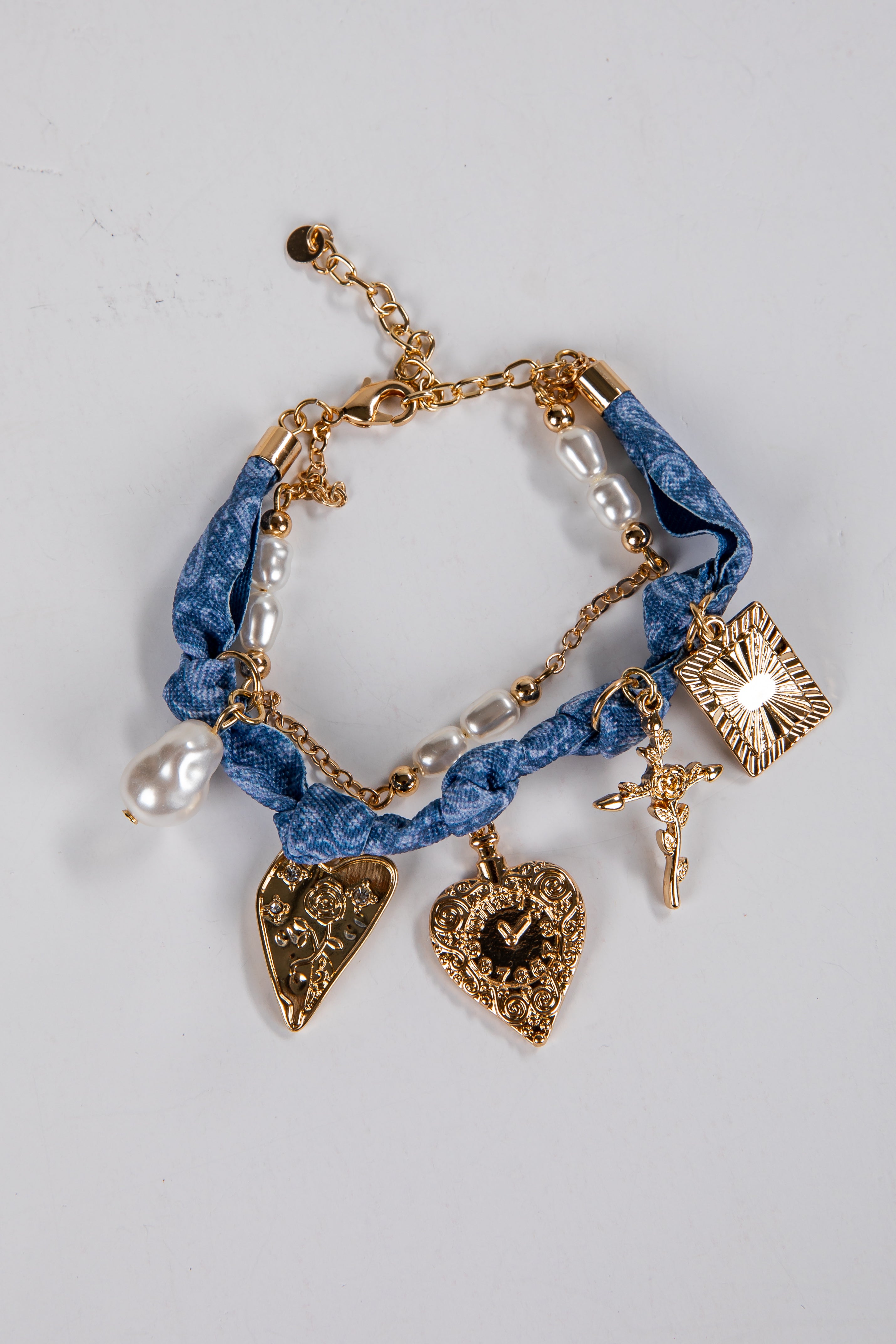 Blue braided bracelet with gold charms and pearls on a light gray background