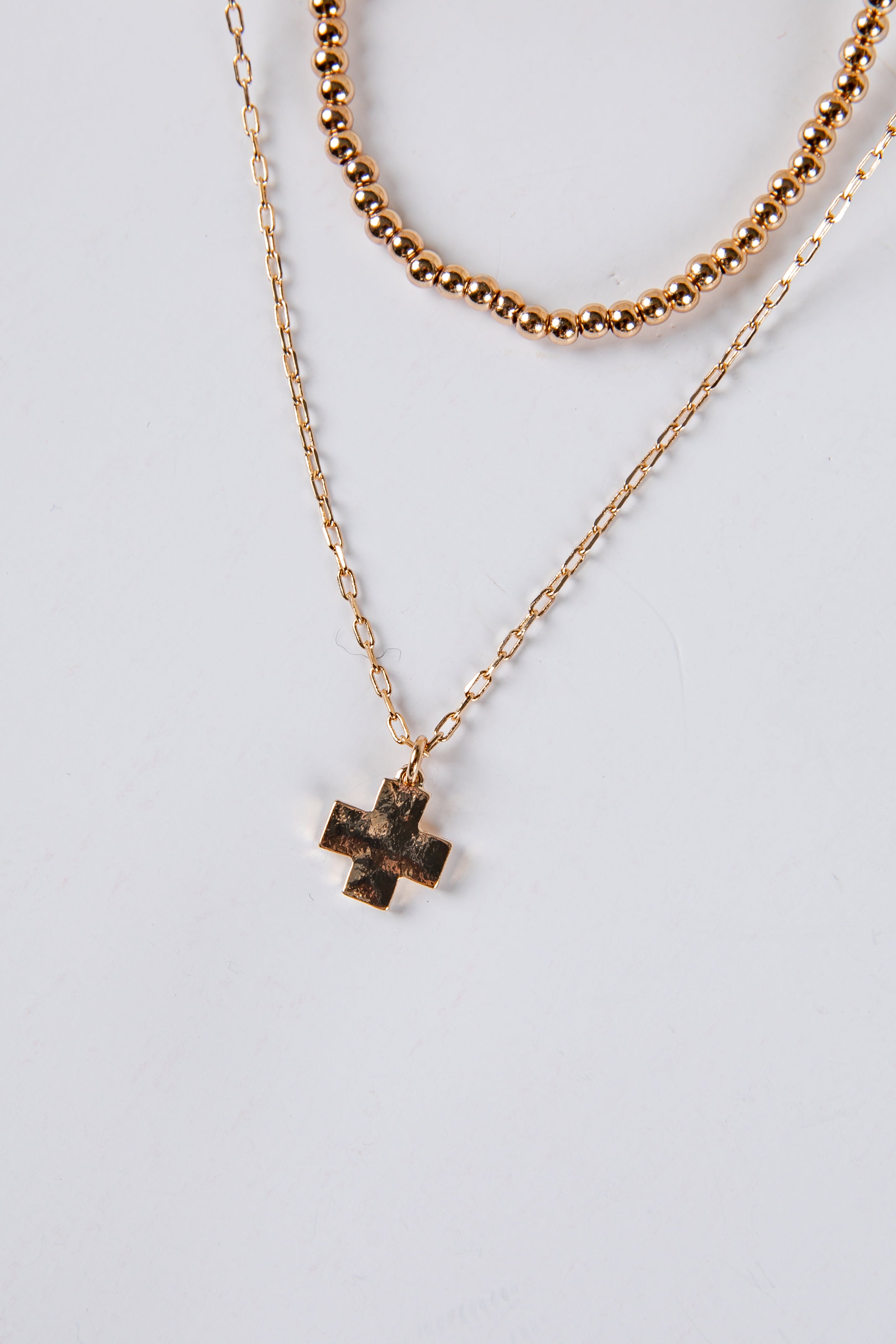 Gold cross necklace and beaded necklace on a light gray background