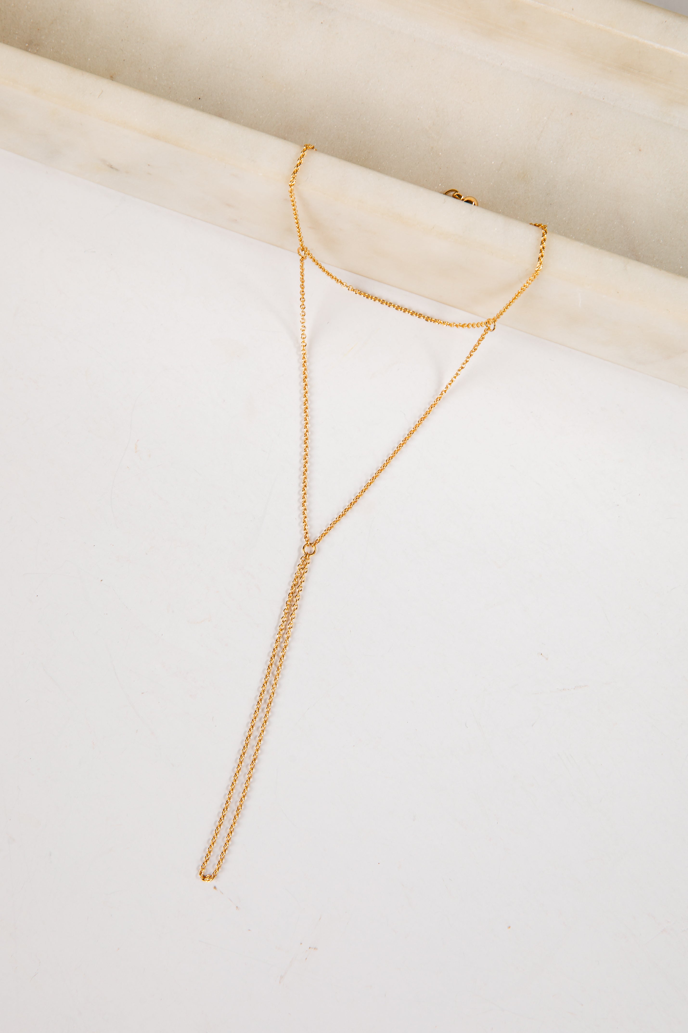 Gold necklace on a white surface with a light wood background