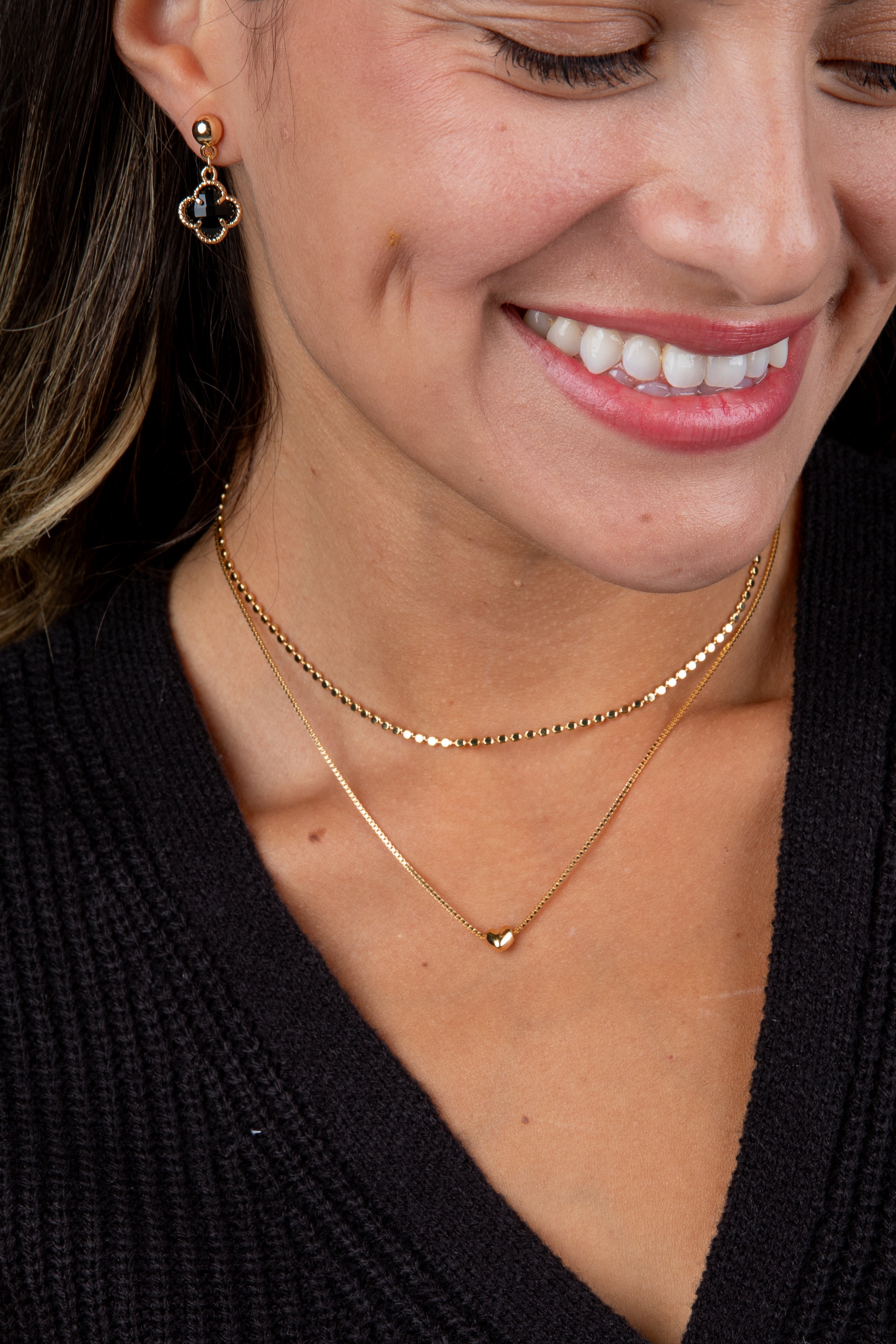 Close-up of a woman wearing gold necklaces and earrings, with a blurred background.