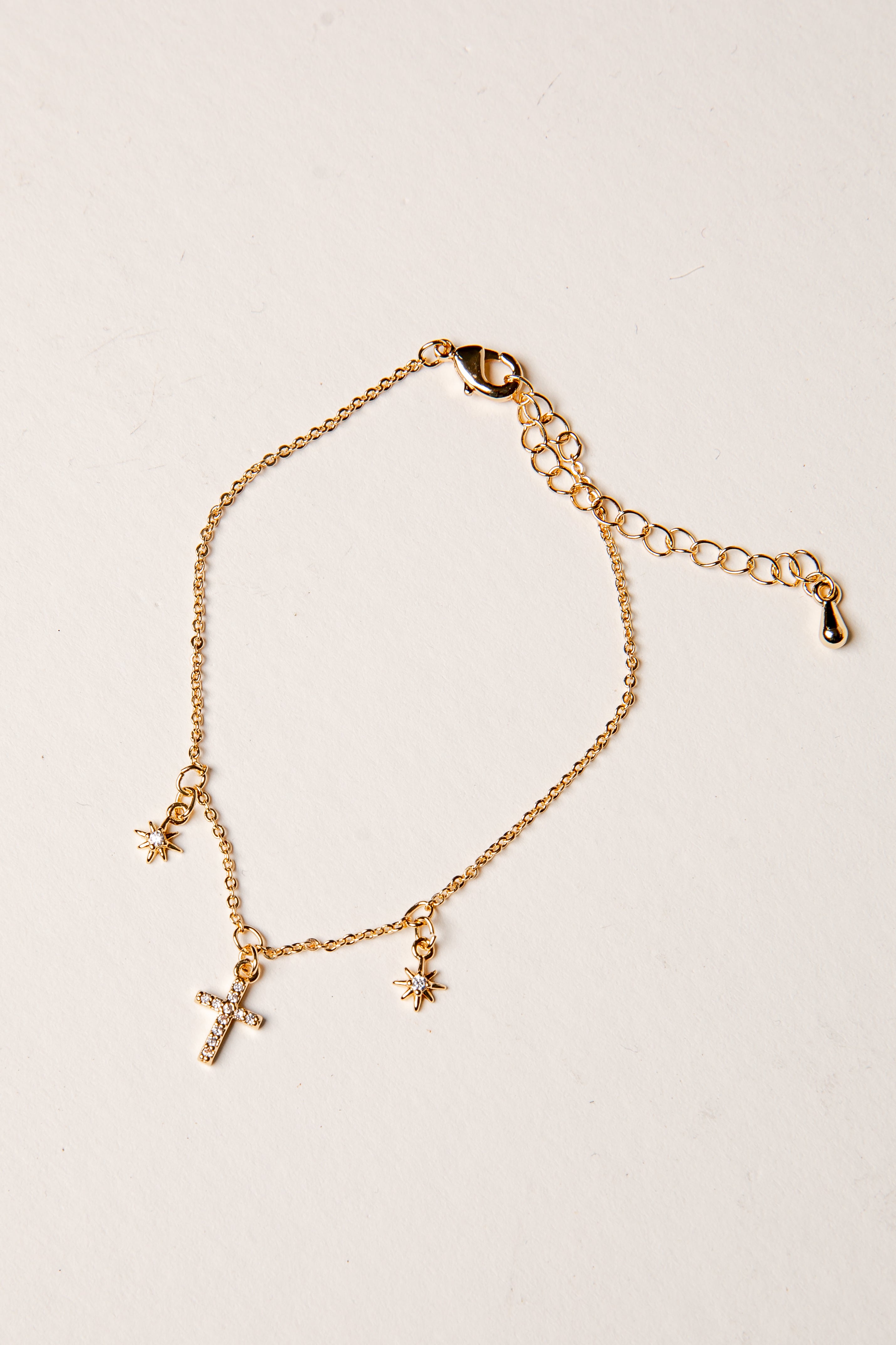 Gold bracelet with a cross and star charm on a beige background