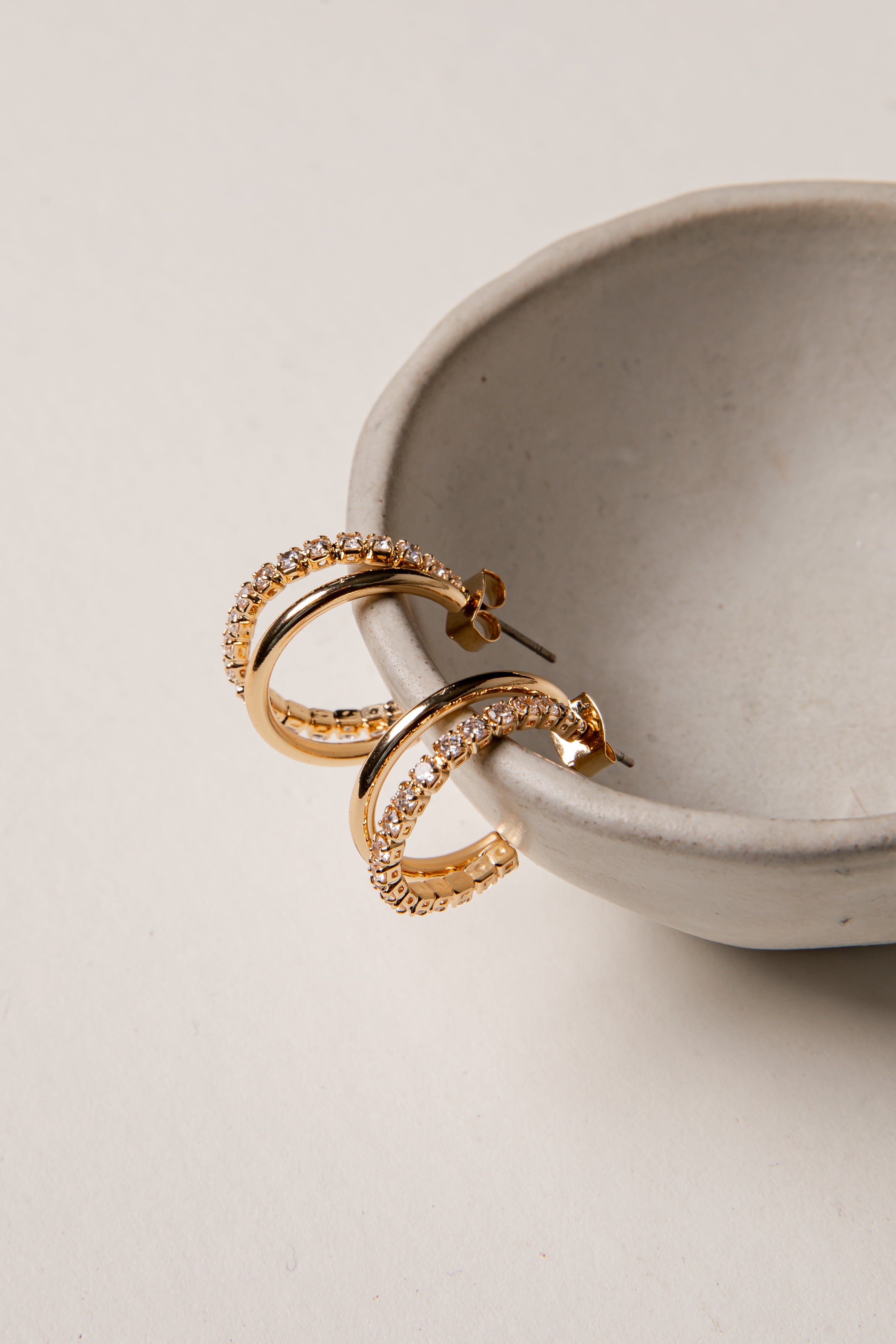 Gold hoop earrings on a light gray surface with a neutral background