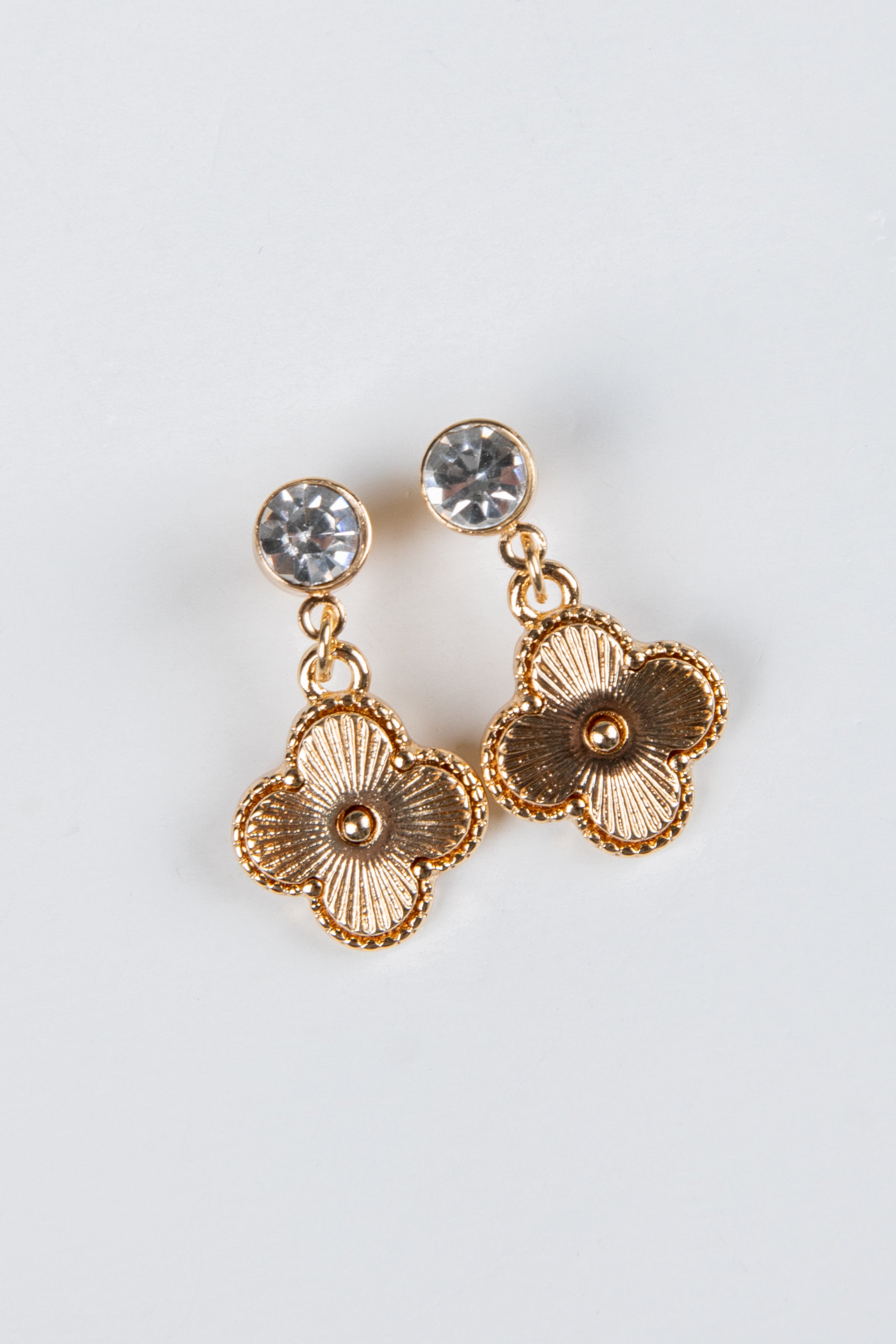 Gold floral earrings with clear gemstones on a light gray background