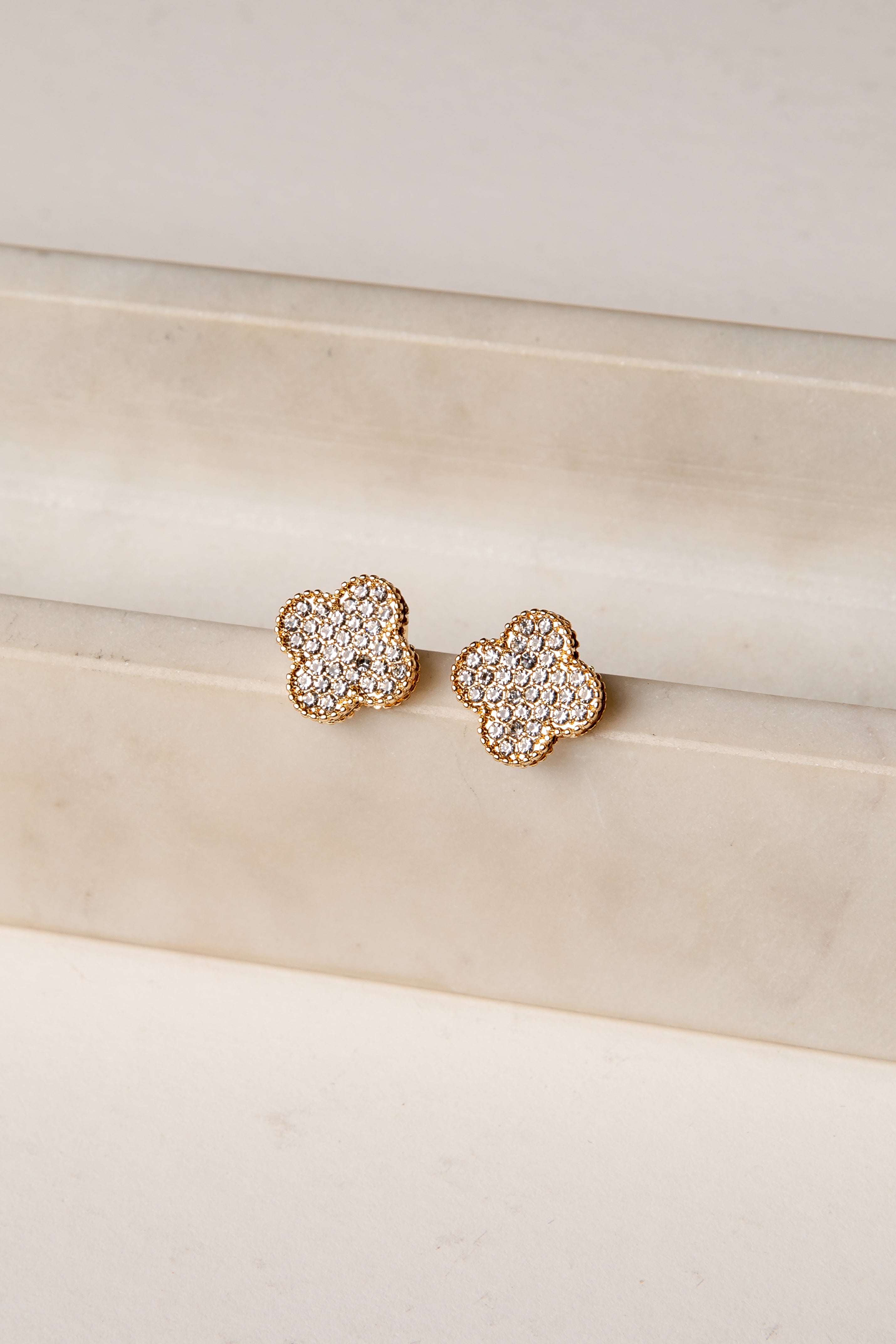 Pair of gold floral earrings with clear gemstones on a beige surface.