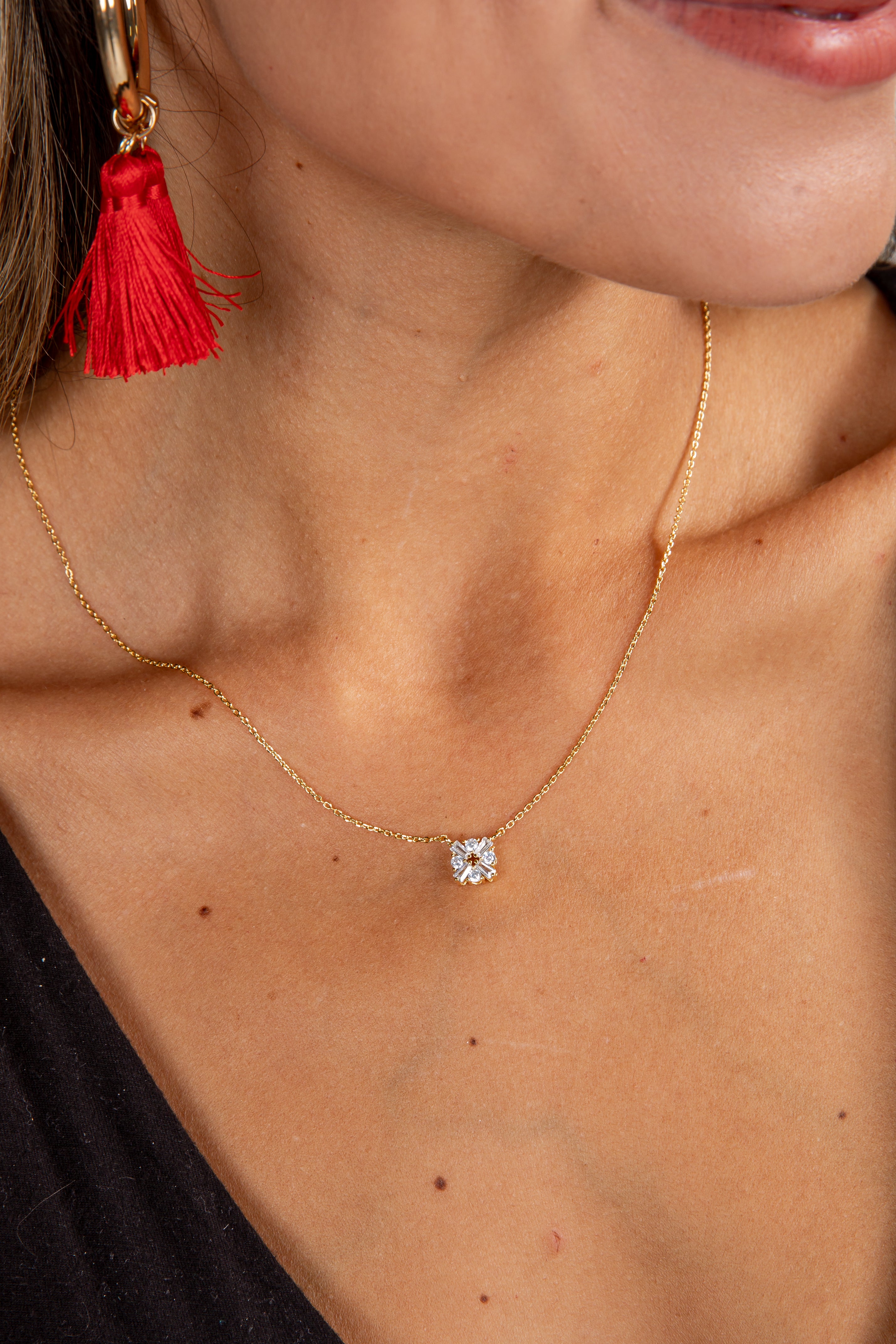 Close-up of a gold necklace with a diamond pendant worn by a person, with a red tassel earring visible.