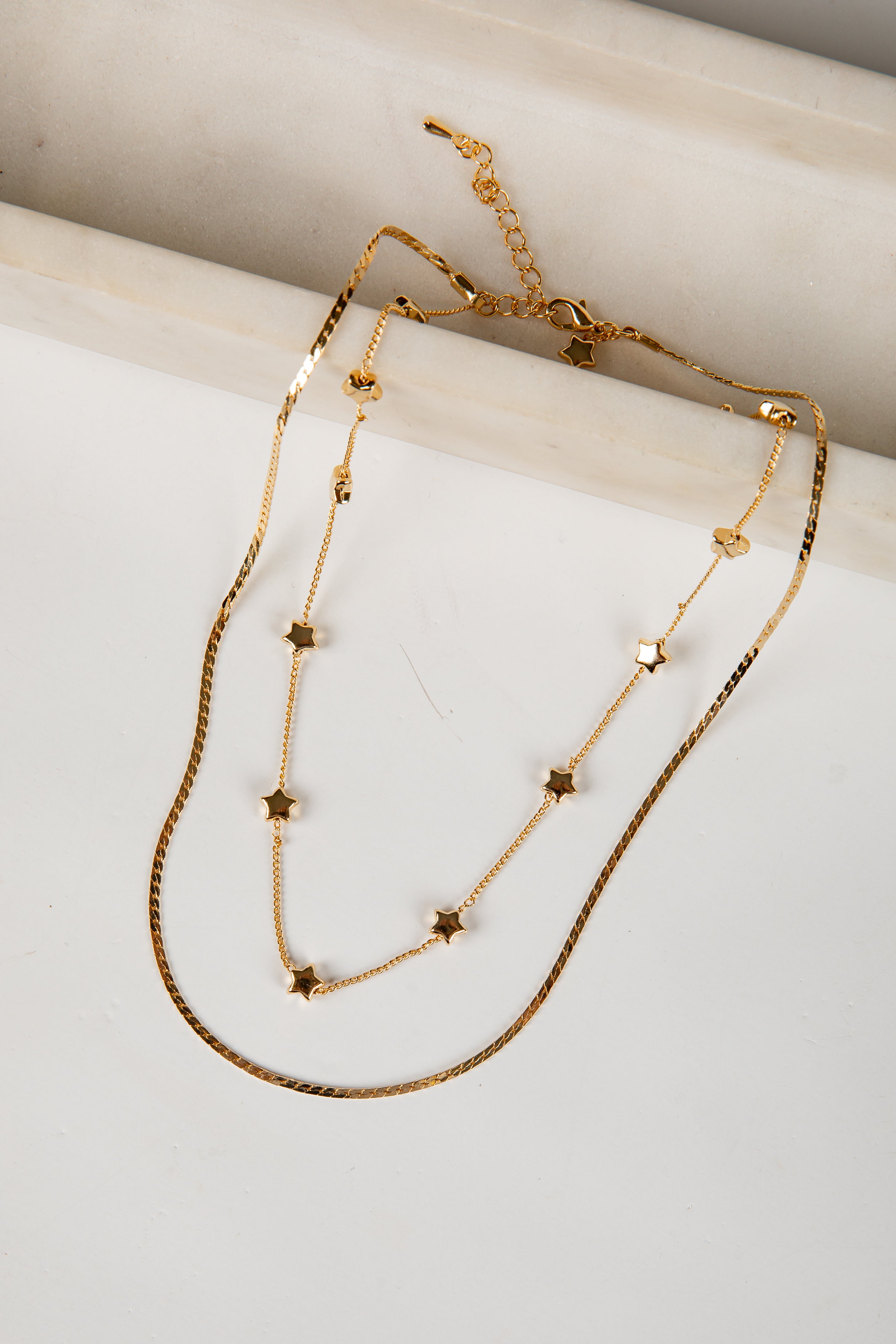 Gold necklace with star-shaped beads on a marble surface