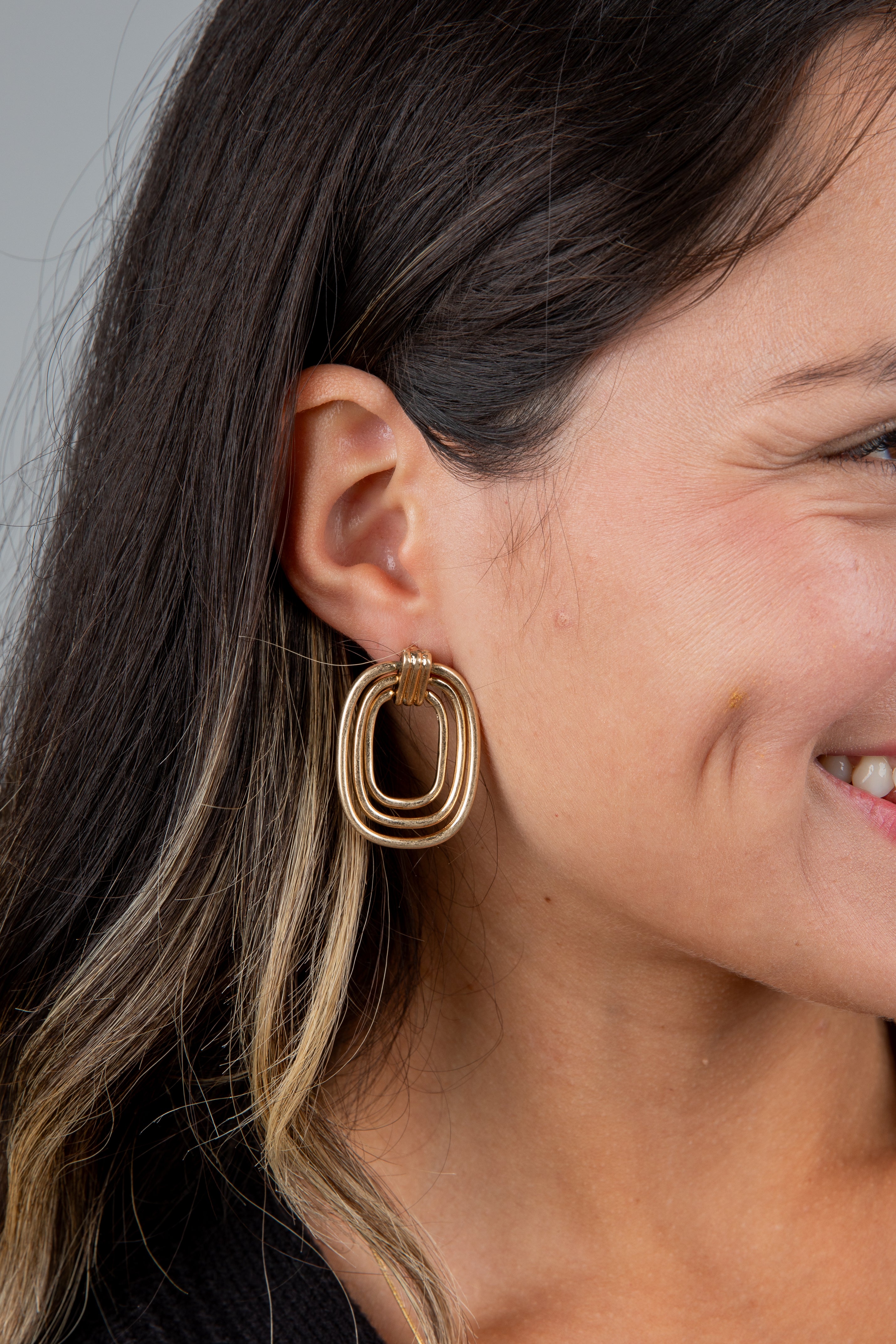 Close-up of a woman wearing gold hoop earrings with a neutral background