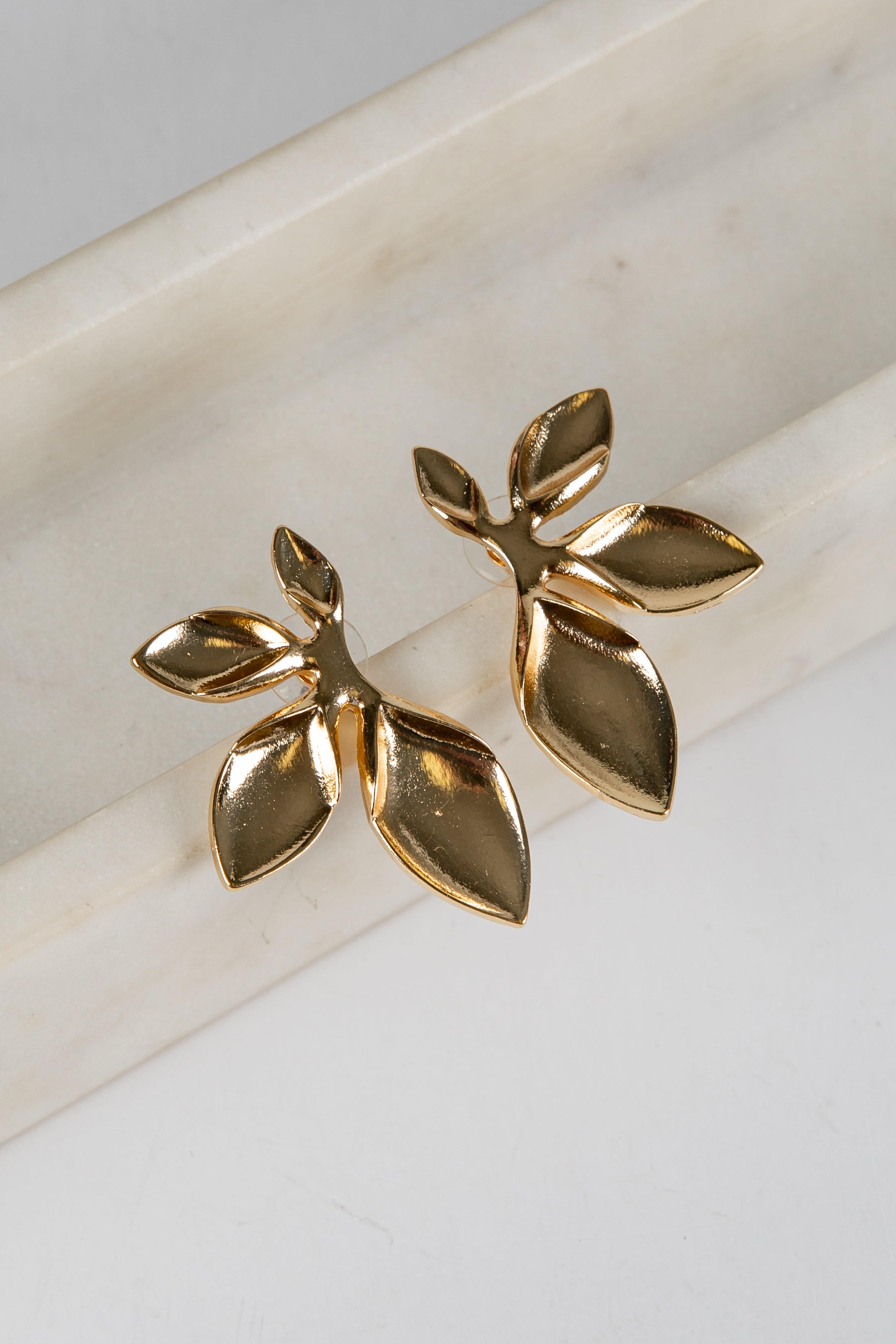 Gold leaf-shaped earrings on a marble surface