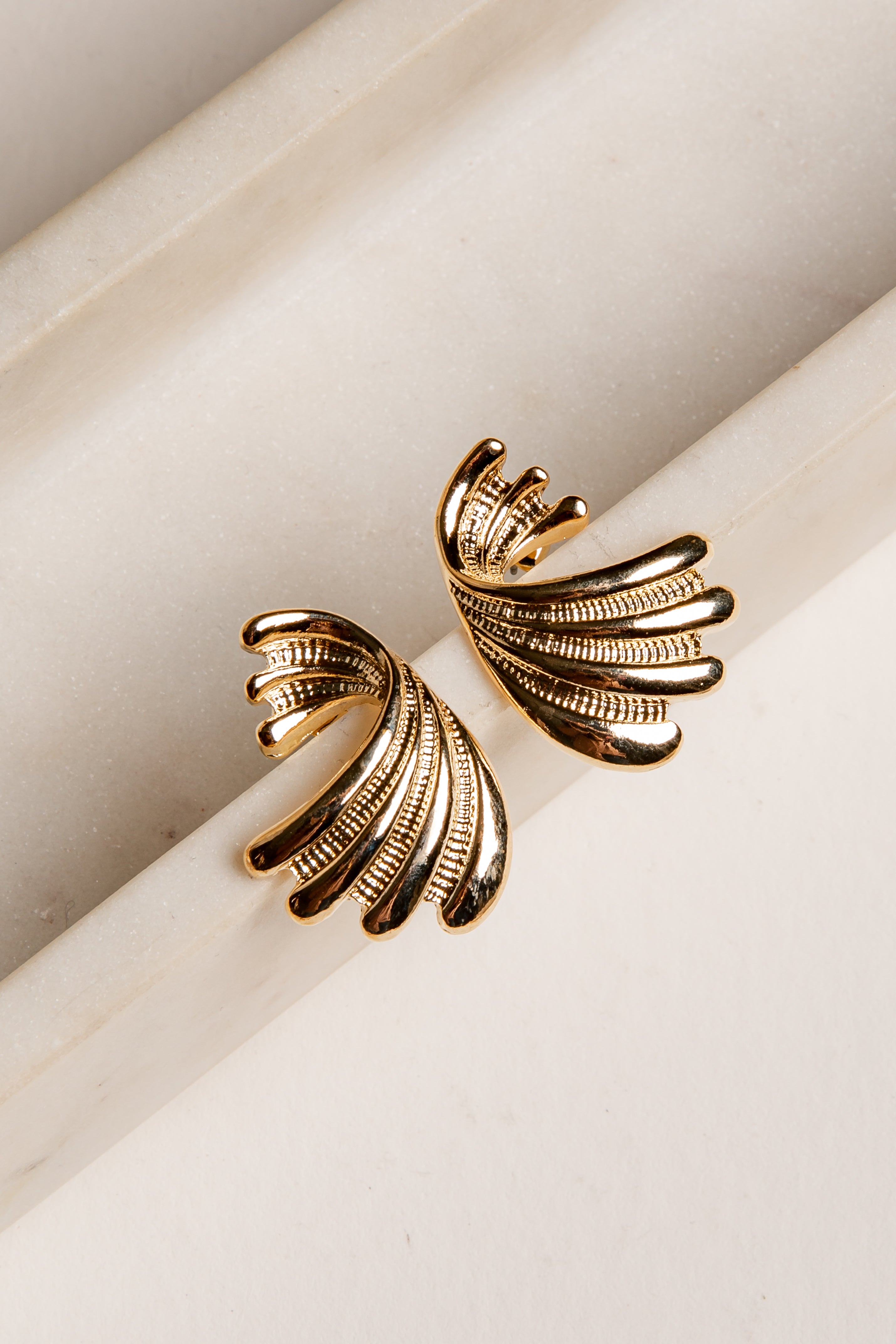 Gold wing-shaped earrings on a light beige surface